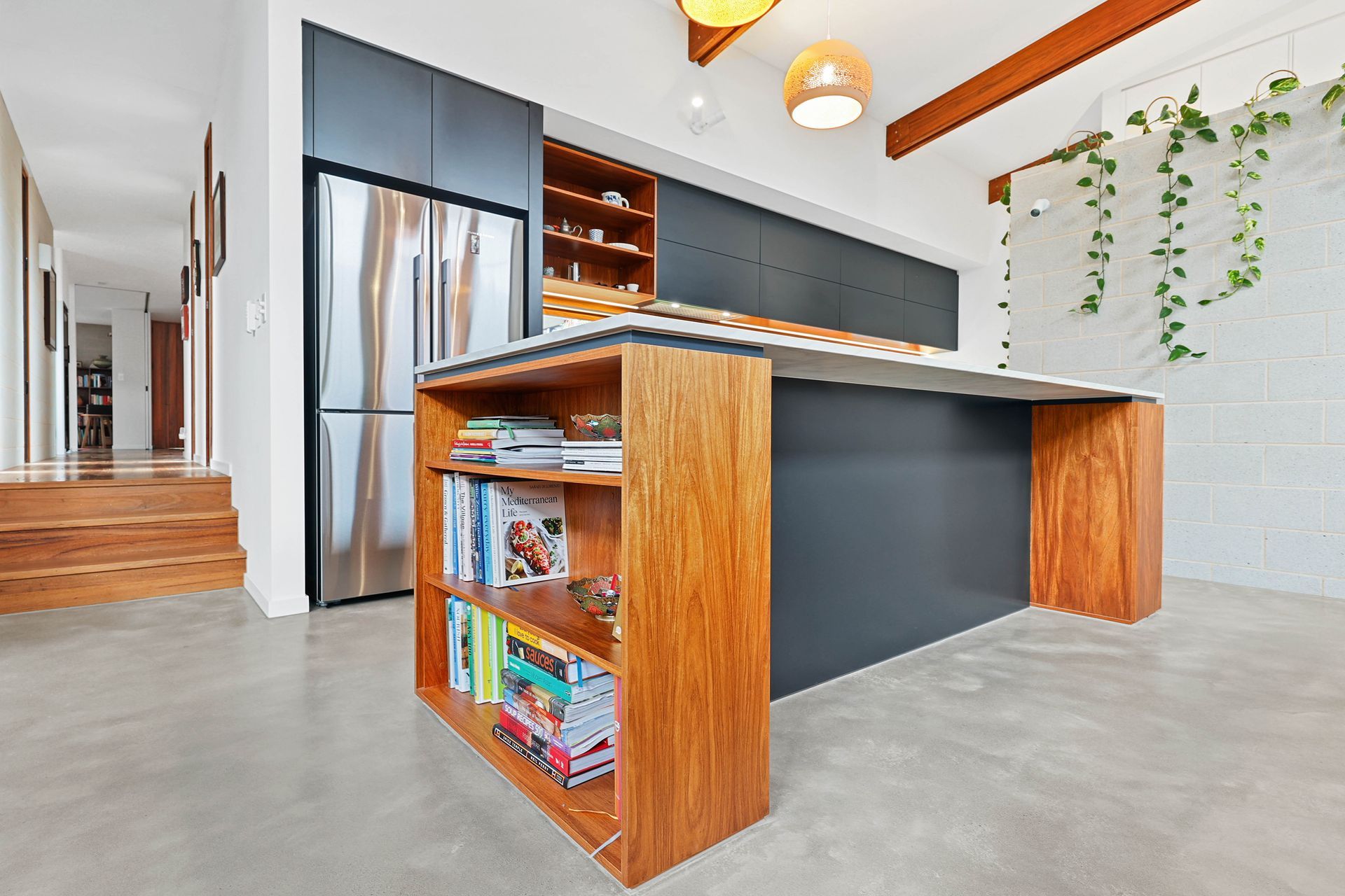 Modern kitchen with dark grey cabinets, wooden island with bookshelves, and stainless steel refrigerator.