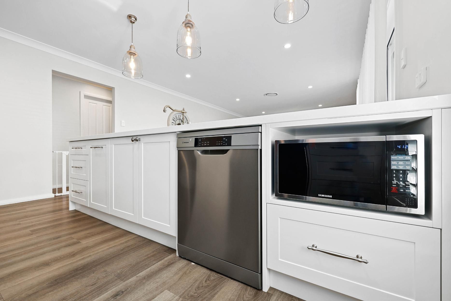 Modern White Kitchen with Stainless Steel Dishwasher and Microwave Built-In. Wooden Floor, Hanging Lights — Above & Beyond Interiors Custom Joinery in Thirlmere, NSW