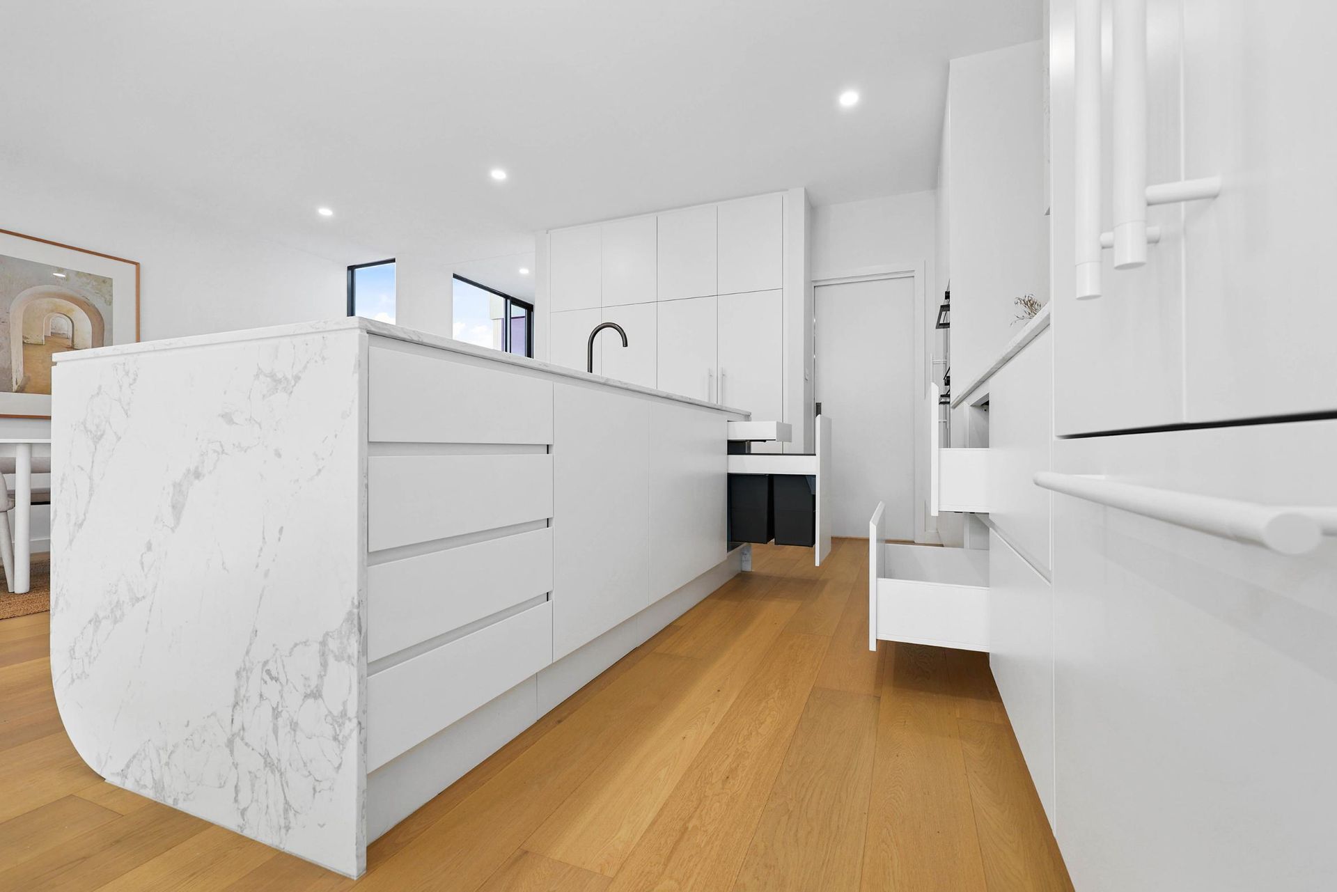 Modern White Kitchen with Marble Island, Wooden Floor, and Black Faucet — Above & Beyond Interiors Custom Joinery in Thirroul, NSW