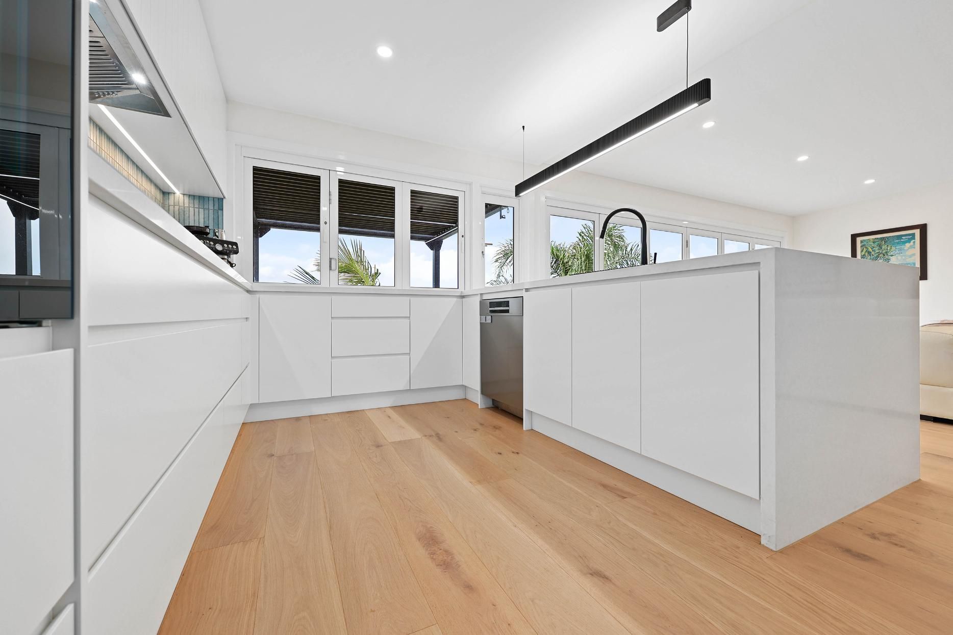 Modern White Kitchen with Hardwood Floors, Island, and Black Pendant Light — Above & Beyond Interiors Custom Joinery in North Curl Curl, NSW