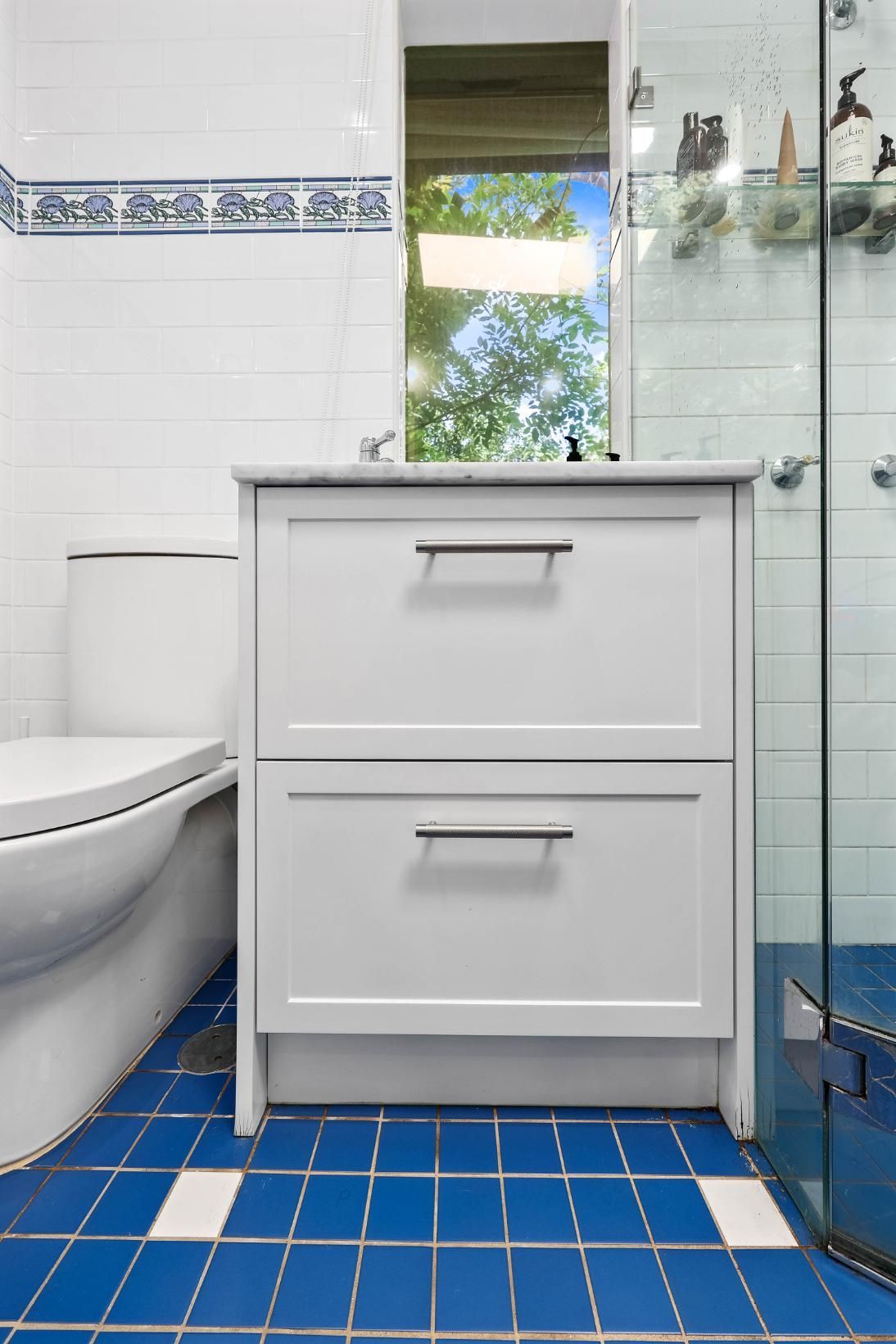 White Bathroom Vanity with Two Drawers and A Blue Tiled Floor. Toilet to The Left, Shower on The Right — Above & Beyond Interiors Custom Joinery in Erskineville, NSW