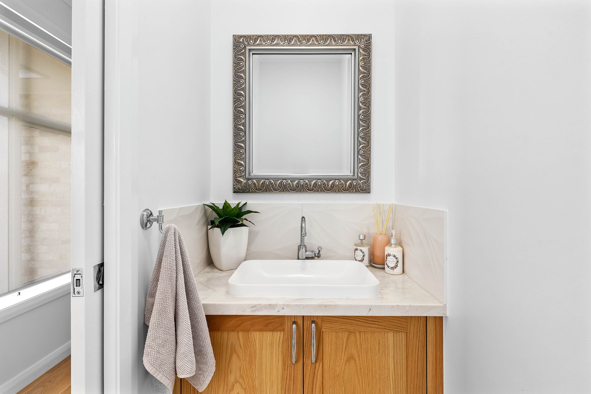 Small bathroom with wooden cabinet, white sink, framed mirror, and a hanging towel — Above & Beyond Interiors Custom Joinery in Bradbury, NSW