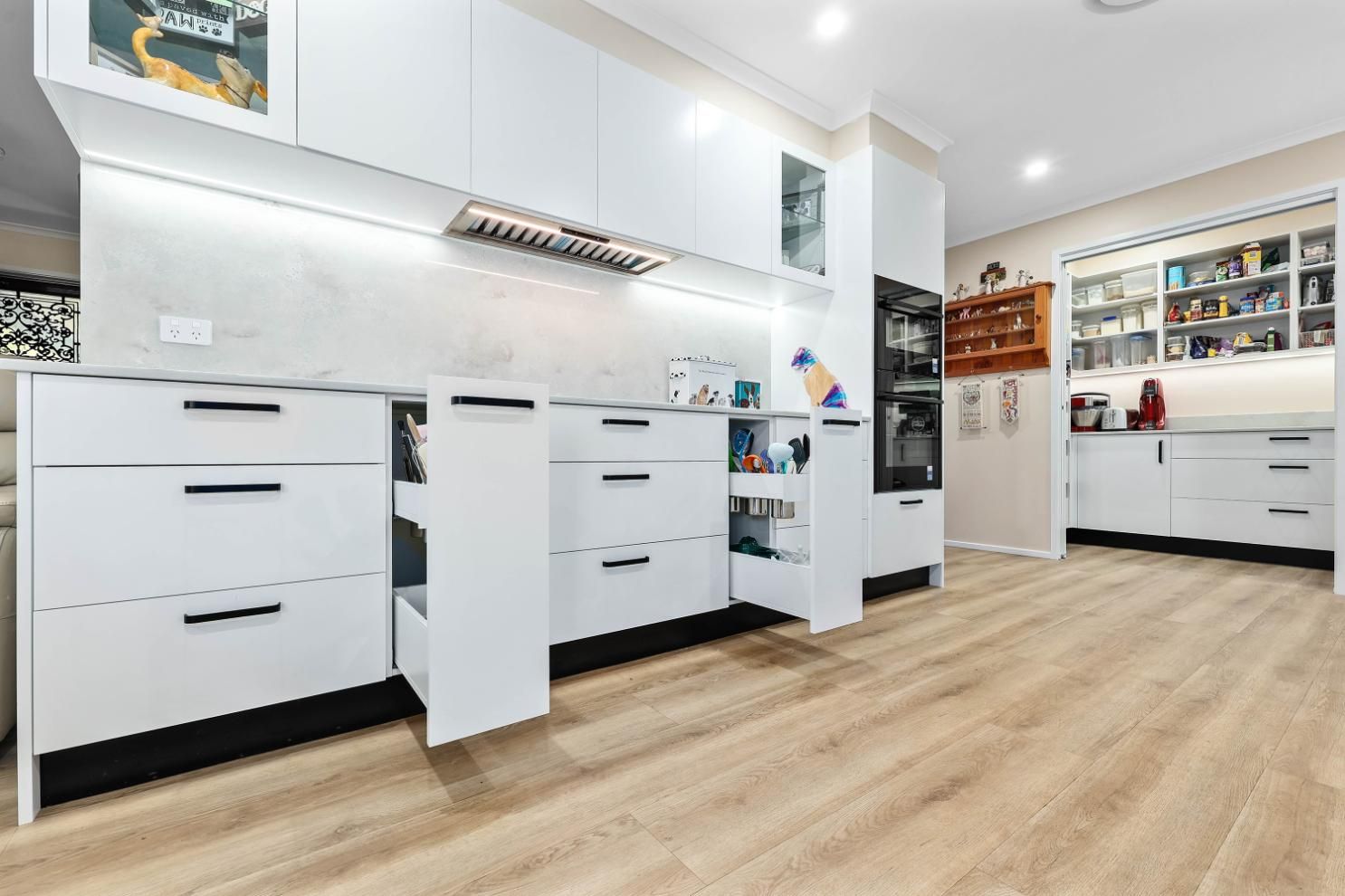 Modern White Kitchen with Open Drawers, Wood-Look Flooring, and Built-In Appliances — Above & Beyond Interiors Custom Joinery in Bradbury, NSW