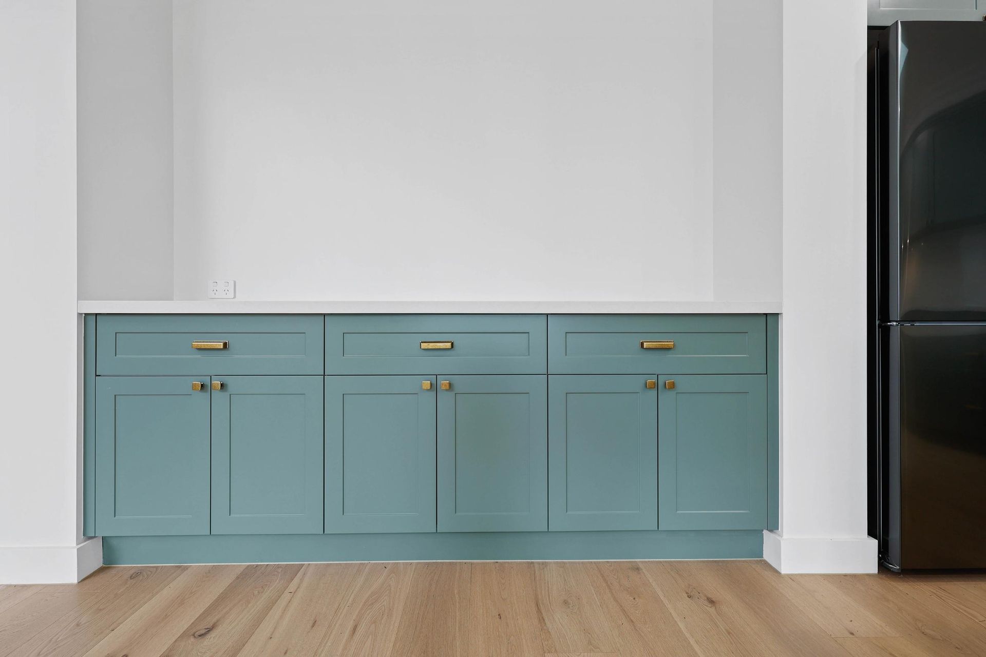 Blue Kitchen Cabinets with Gold Hardware Under a White Countertop and Refrigerator on Right — Above & Beyond Interiors Custom Joinery in Appin, NSW