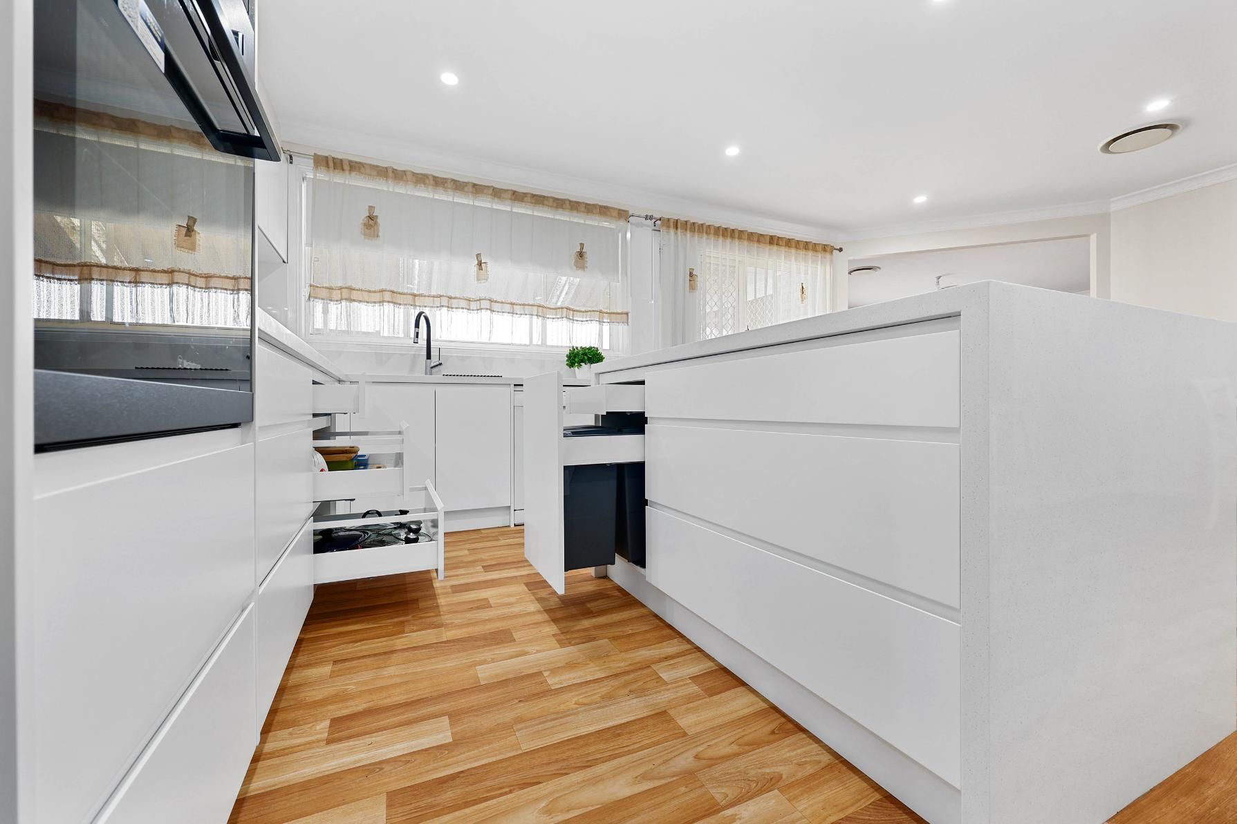 Modern White Kitchen with Wood Floors and A Large Island — Above & Beyond Interiors Custom Joinery in Narellan Vale, NSW
