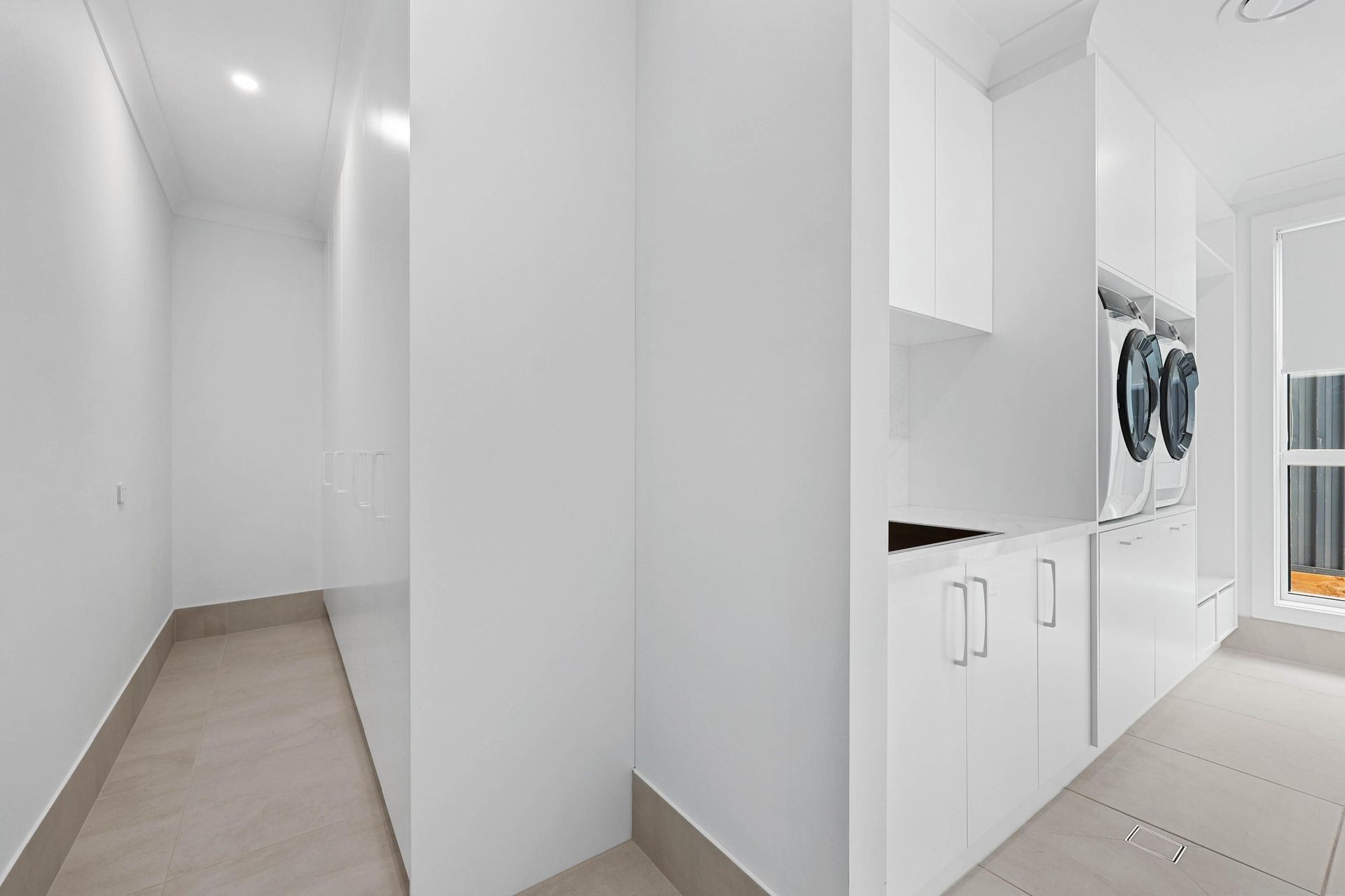 Bright White Laundry Room with Washing Machine and Built-In Cabinets and A Narrow Hallway — Above & Beyond Interiors Custom Joinery in Currans Hill, NSW