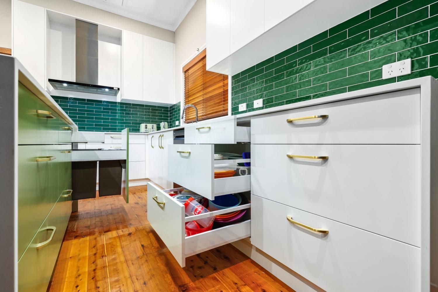 Modern White Kitchen with Open Drawers, Gold Handles, Green Tile Backsplash, and Wooden Floor — Above & Beyond Interiors Custom Joinery in Minto, NSW
