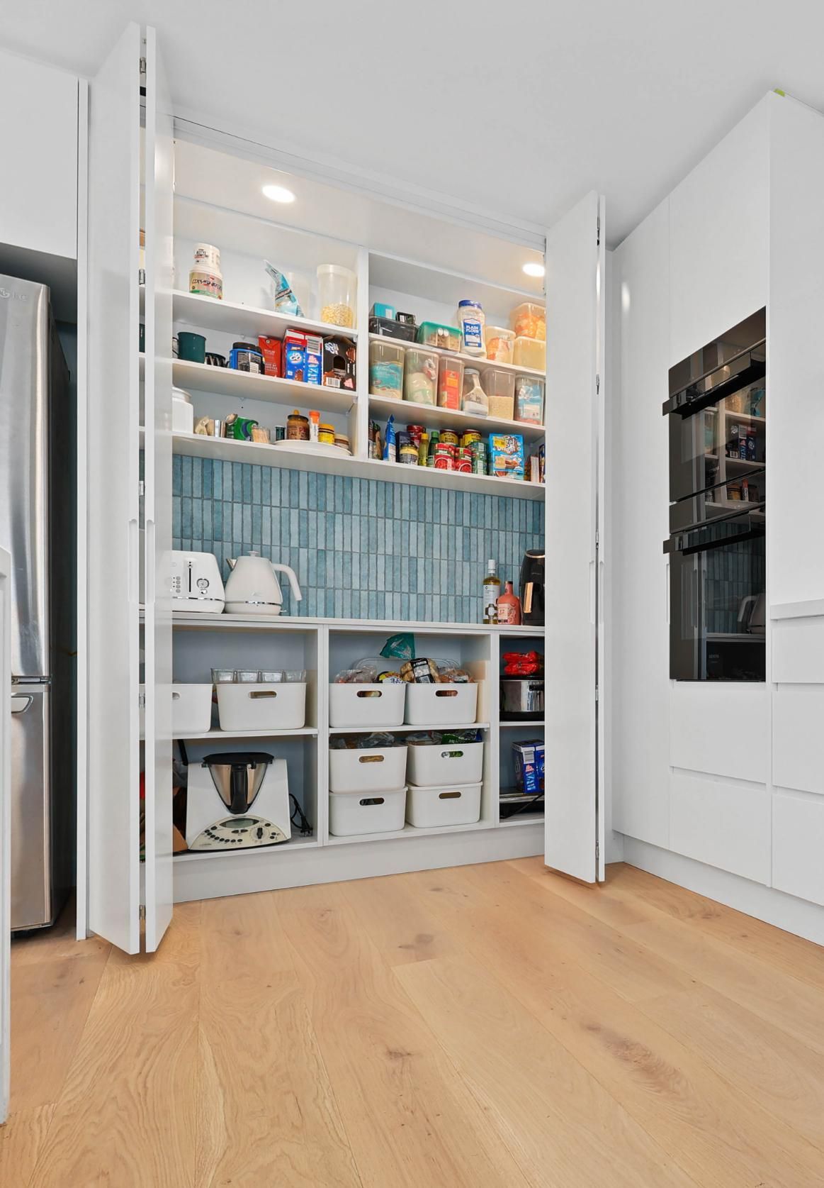White Pantry with Open Doors, Shelves Stocked with Food and Appliances. Light Wood Floor — Above & Beyond Interiors Custom Joinery in North Curl Curl, NSW