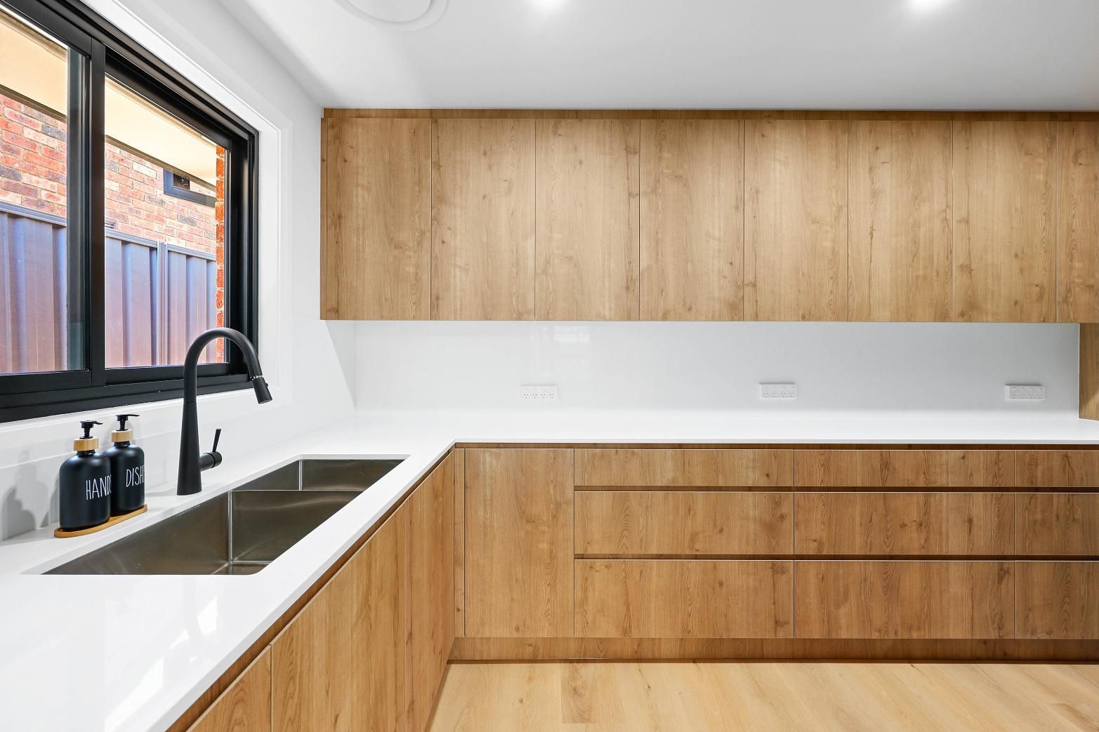 Modern Kitchen with Wood Grain Cabinets, White Countertops, and A Stainless Steel Sink Near a Window — Above & Beyond Interiors Custom Joinery in Abbortsbury, NSW