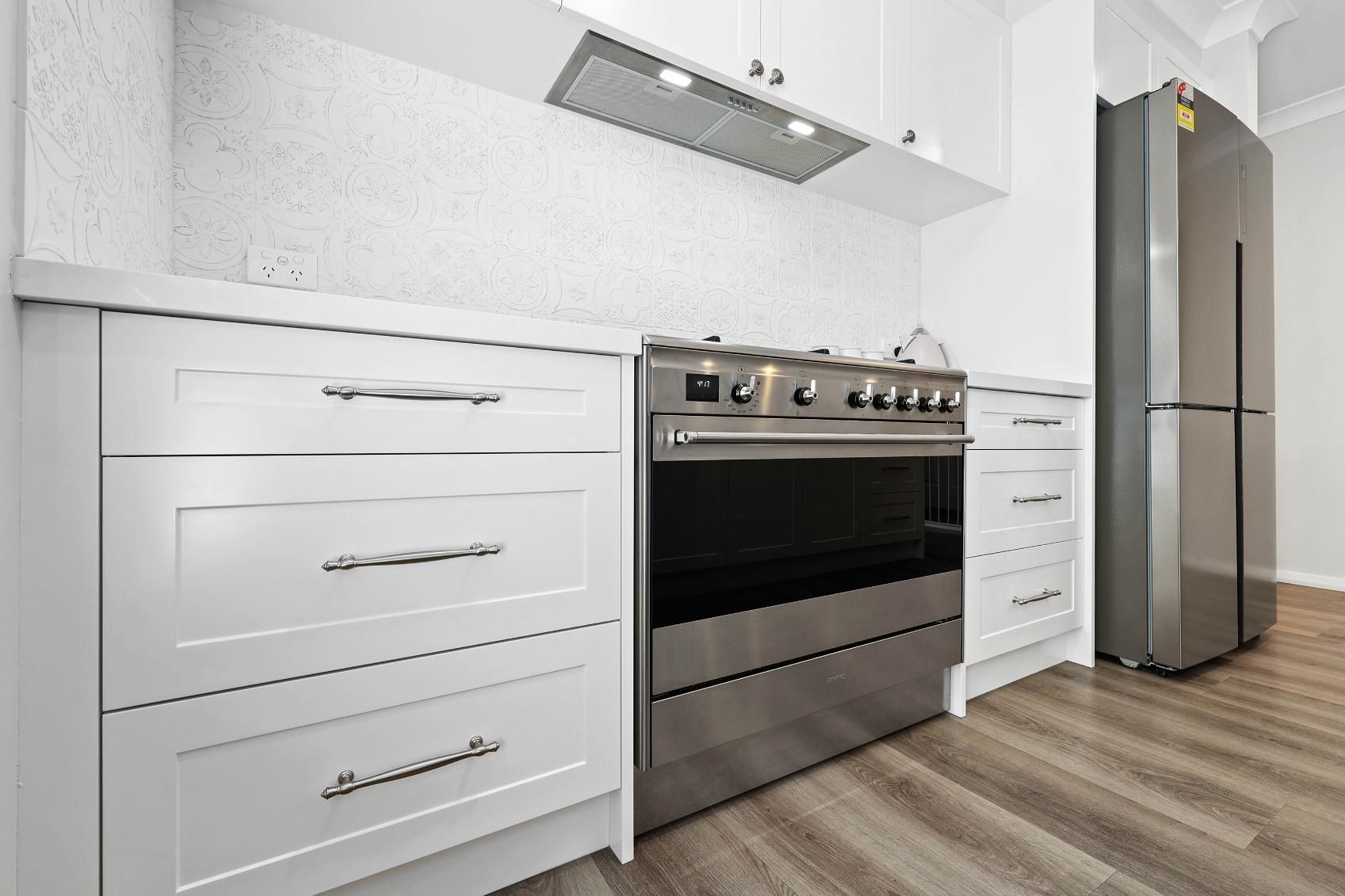 Modern White Kitchen with Stainless Steel Appliances and Wooden Floor — Above & Beyond Interiors Custom Joinery in Thirlmere, NSW
