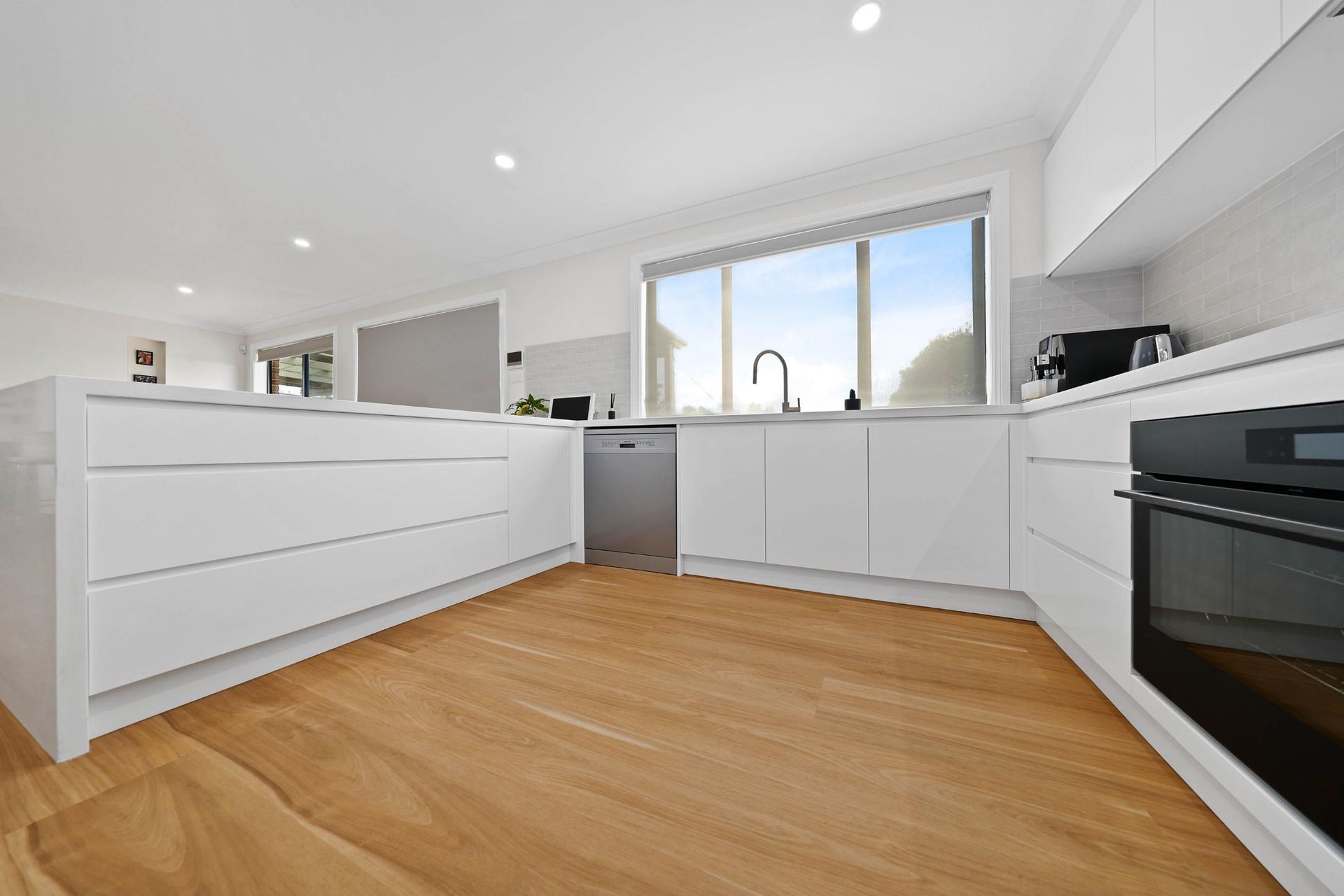 Bright Modern Kitchen with White Cabinets, Island, and Wood Floors — Above & Beyond Interiors Custom Joinery in Mount Anna, NSW