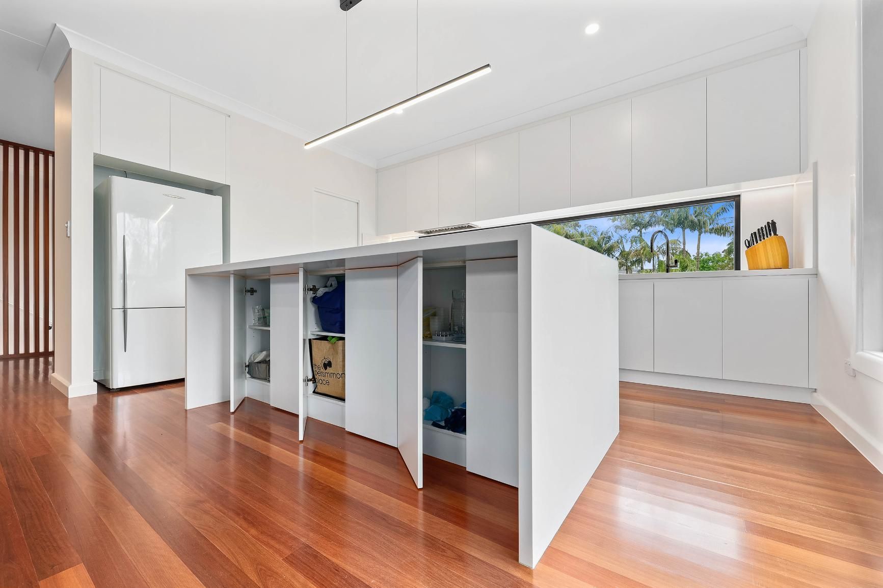 Modern White Kitchen with Large Island and Storage, Hardwood Floors, and Overhead Lighting — Above & Beyond Interiors Custom Joinery in Killara, NSW