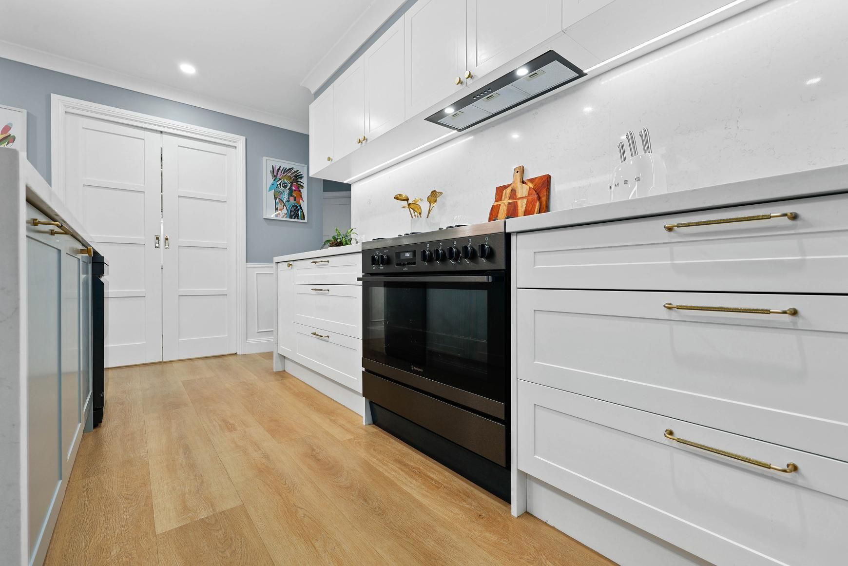 White Kitchen with Wooden Floors, Cabinets, Black Oven, and Light Blue Walls — Above & Beyond Interiors Custom Joinery in Harrington Park, NSW