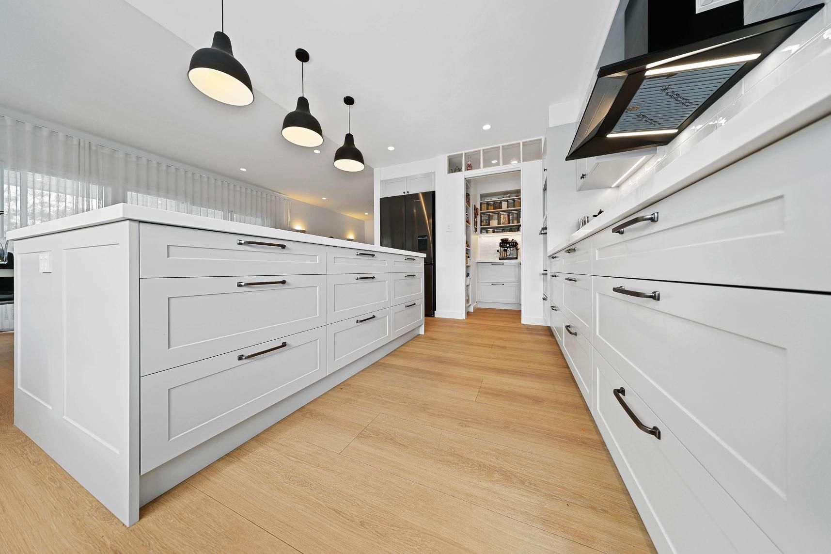 Modern White Kitchen with Island, Wood Floor, Black Pendant Lights, and Appliances — Above & Beyond Interiors Custom Joinery in Yowie Bay, NSW