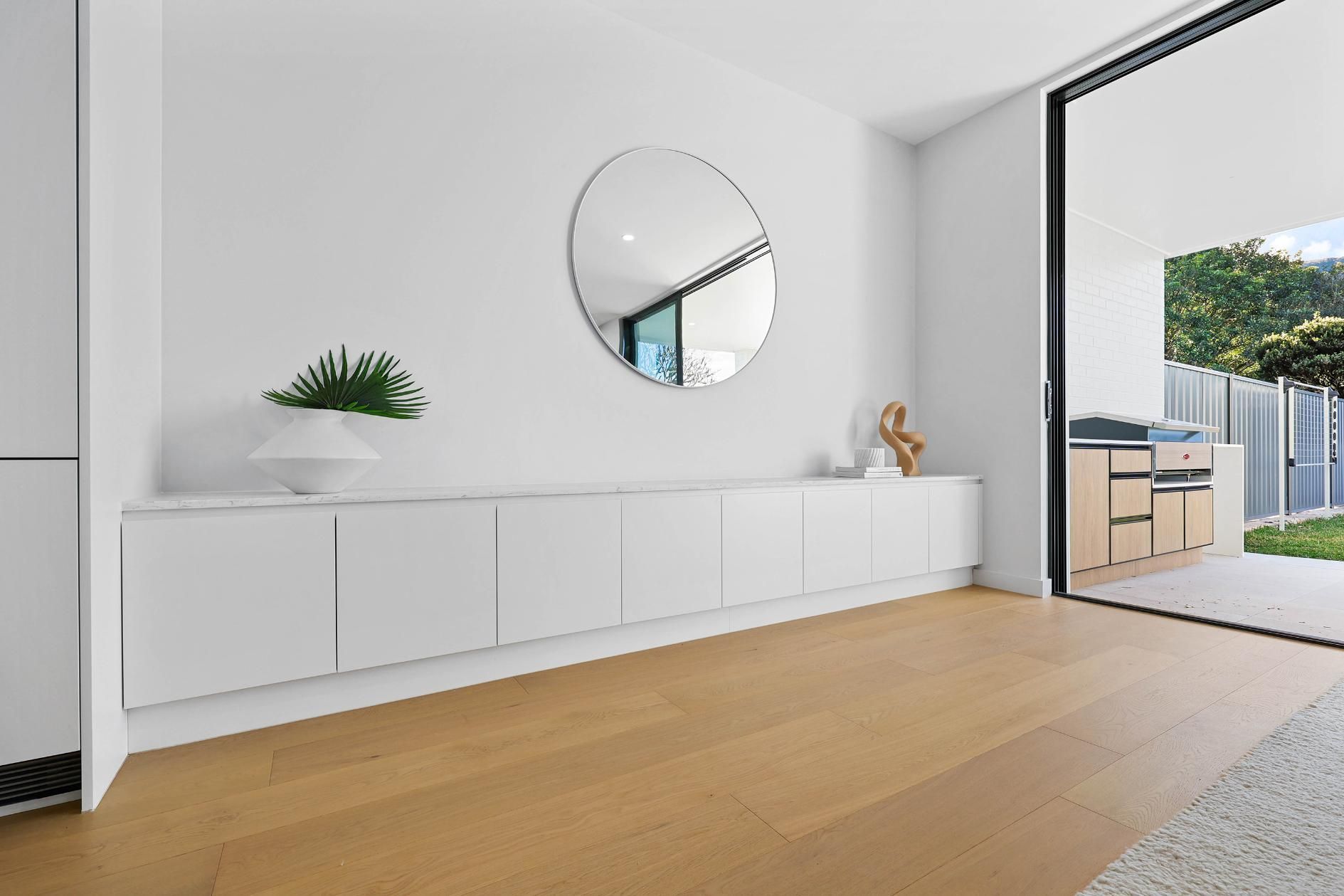 White Wall with A Floating Cabinet and Round Mirror; Open Sliding Door to Patio — Above & Beyond Interiors Custom Joinery in Thirroul, NSW