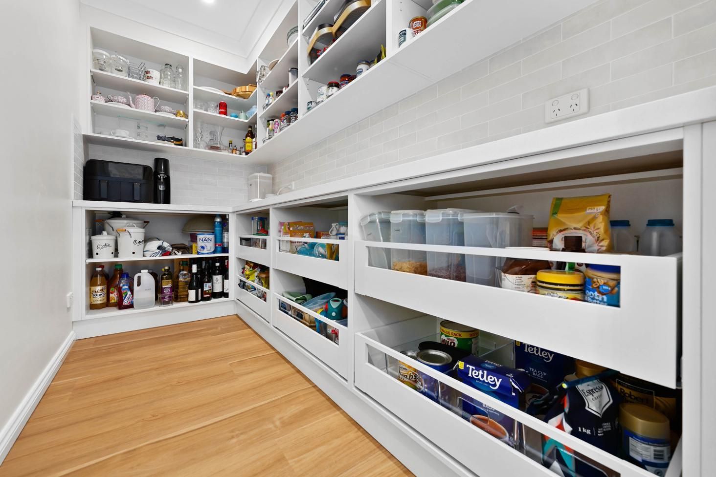 Pantry with White Shelves and Pull-Out Drawers Filled with Food Items on Wood Floor — Above & Beyond Interiors Custom Joinery in Mount Anna, NSW