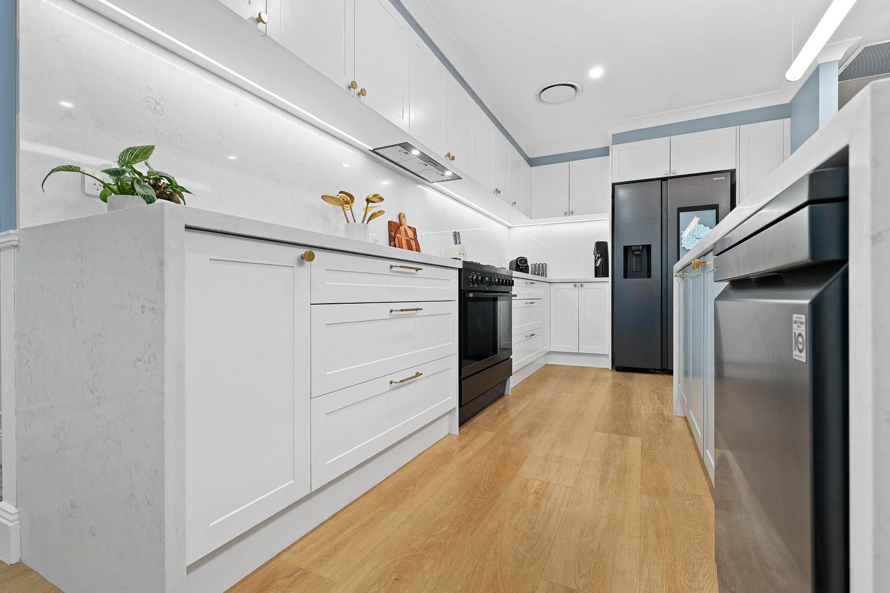Modern White Kitchen with Light Wood Floors, Featuring a Black Oven and Fridge — Above & Beyond Interiors Custom Joinery in Harrington Park, NSW