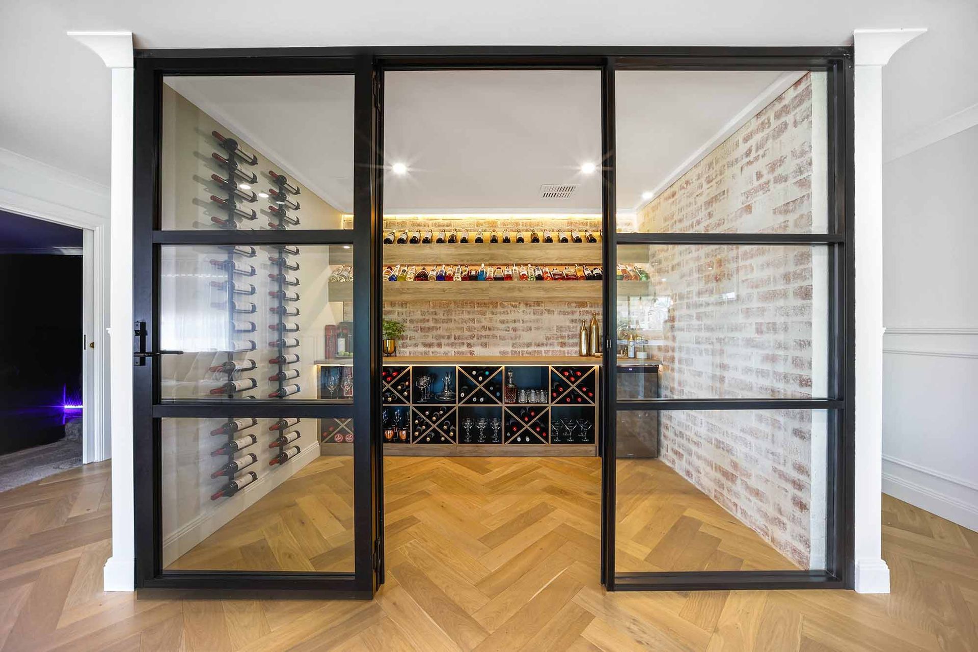 Glass-walled wine cellar with black frames, exposed brick, and herringbone floors — Above & Beyond Interiors Custom Joinery in Bellambi, NSW