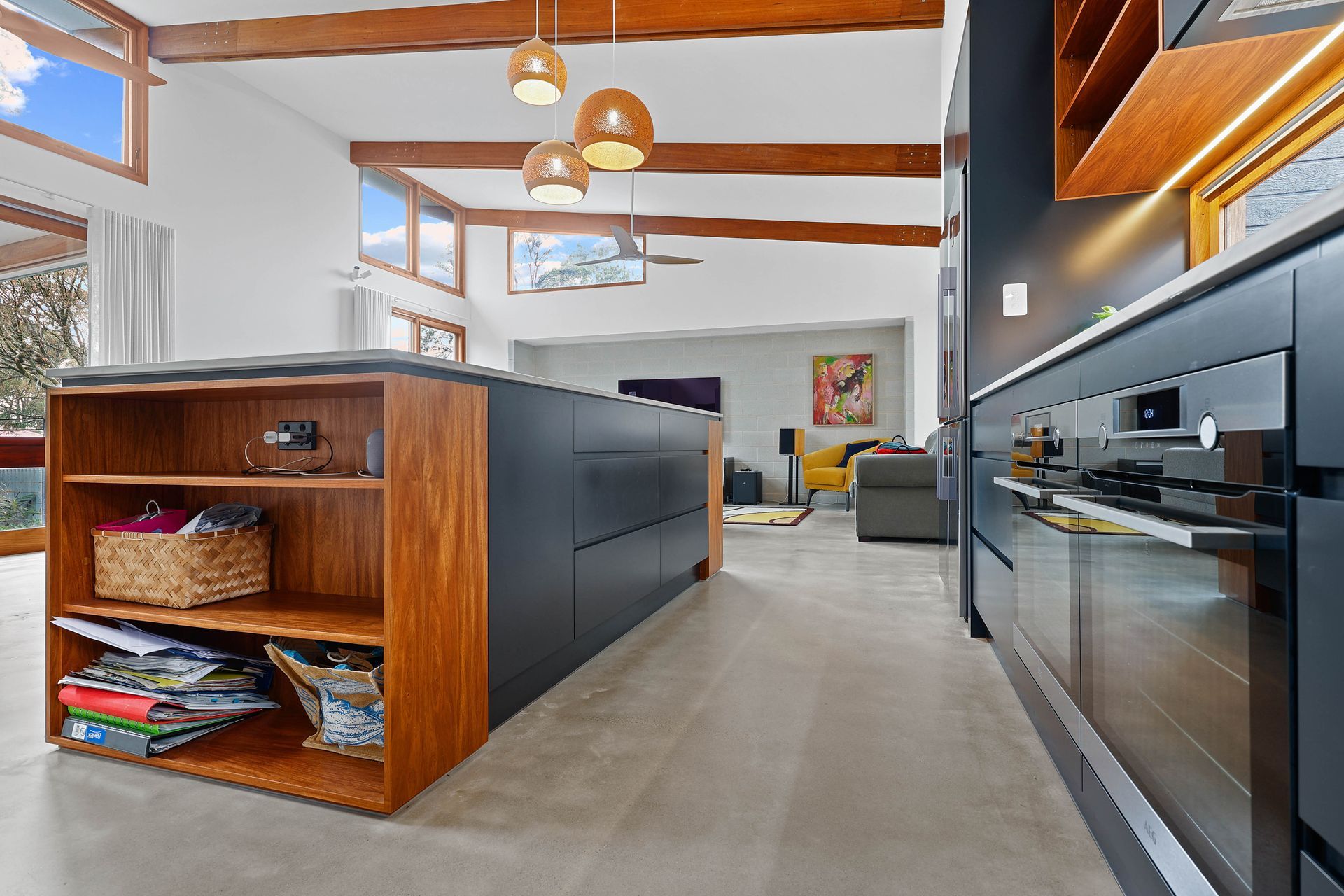 Modern kitchen with a dark island and wood shelves, open to a living room with a yellow armchair.