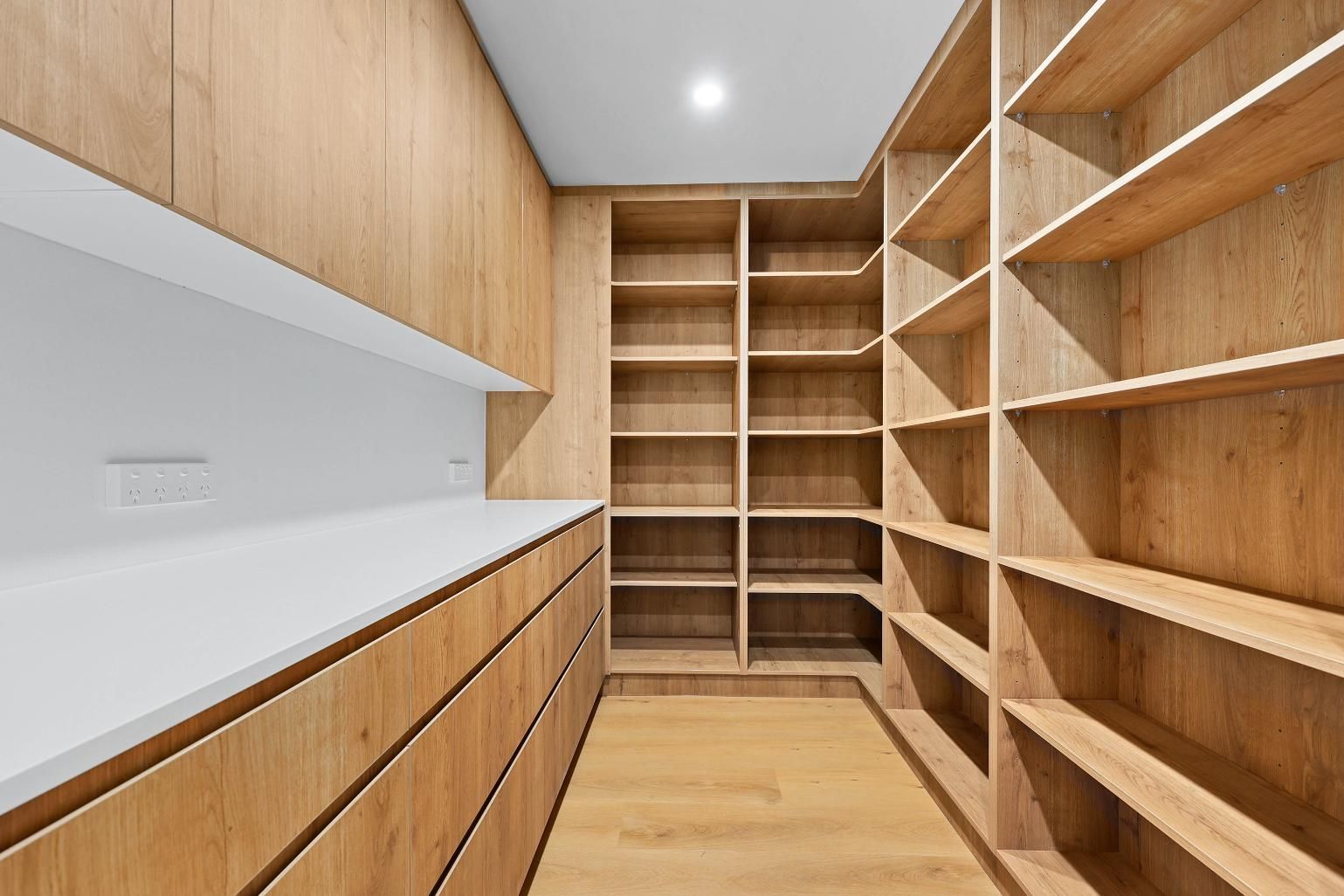 A Walk-In Pantry with Light Wood Shelves and Cabinetry, Featuring a Countertop and Recessed Lighting — Above & Beyond Interiors Custom Joinery in Abbortsbury, NSW