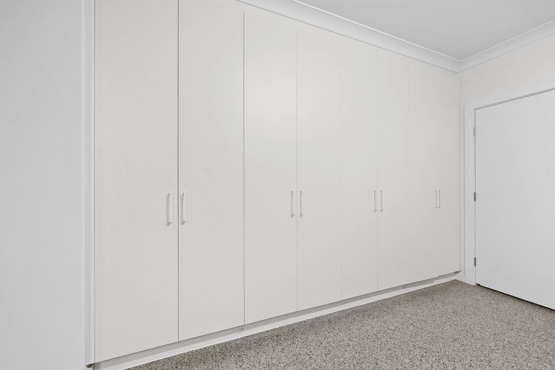 White Built-In Cabinets Line a Wall. a Door Is to The Right. the Floor Is Light-Colored Concrete — Above & Beyond Interiors Custom Joinery in Currans Hill, NSW