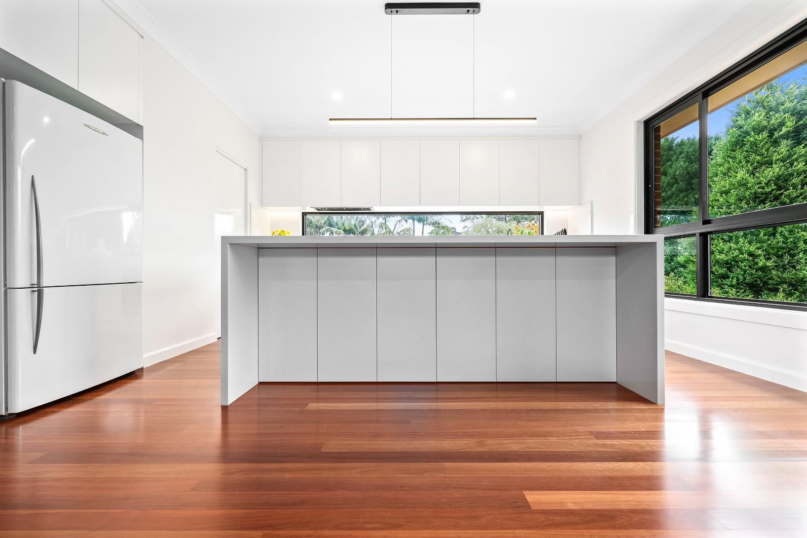 Modern White Kitchen with An Island, a Window with Greenery, and Wood Floors — Above & Beyond Interiors Custom Joinery in Killara, NSW