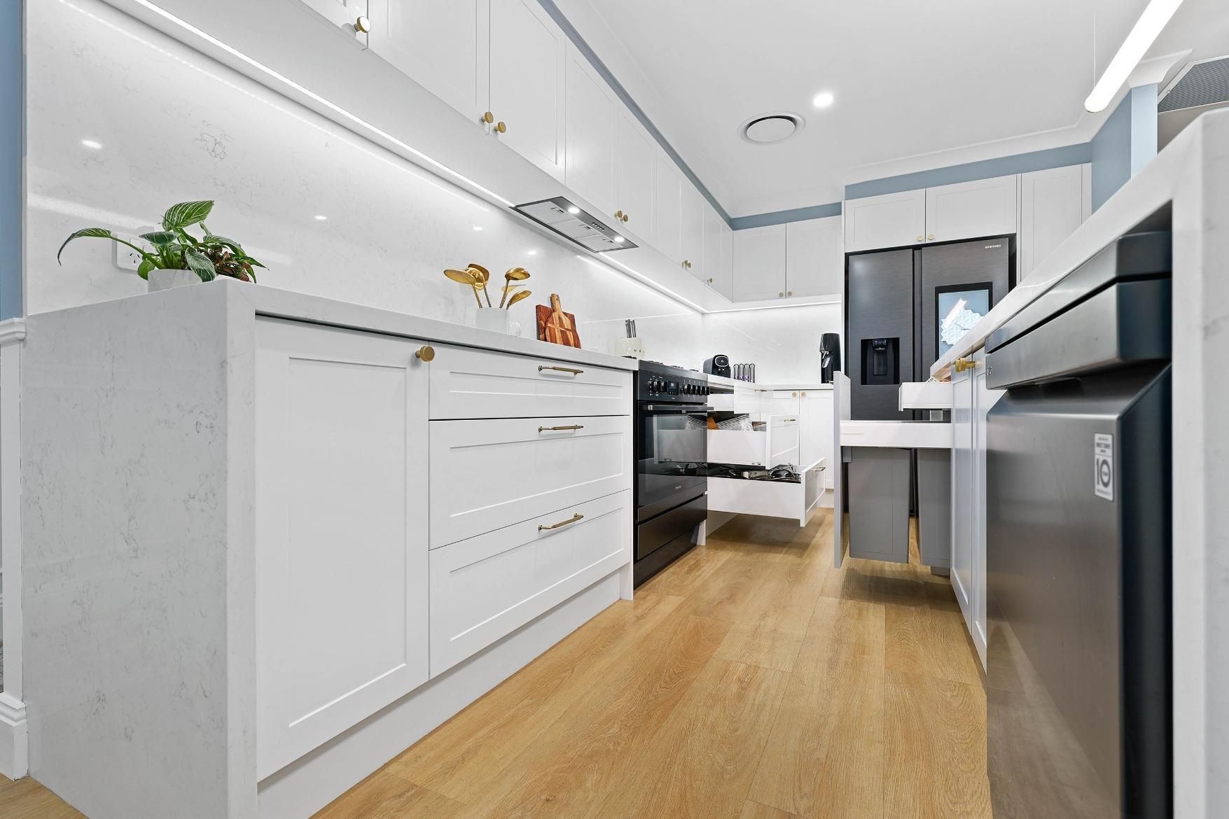 Modern White Kitchen with Wooden Floor, Black Stove, and Stainless Steel Appliances — Above & Beyond Interiors Custom Joinery in Harrington Park, NSW