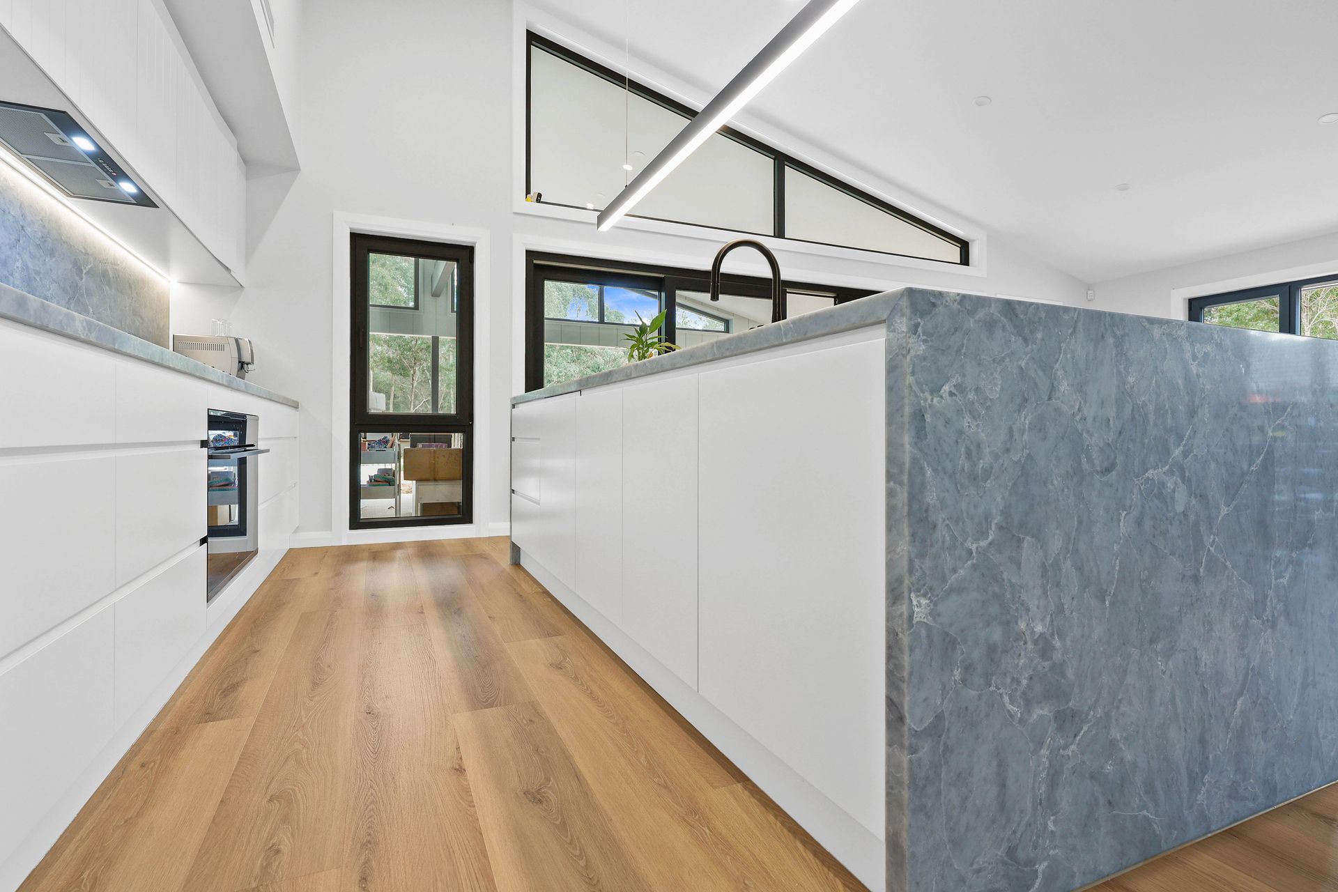 Modern kitchen with white cabinets, grey island, and wood flooring — Above & Beyond Interiors Custom Joinery in Bellambi, NSW