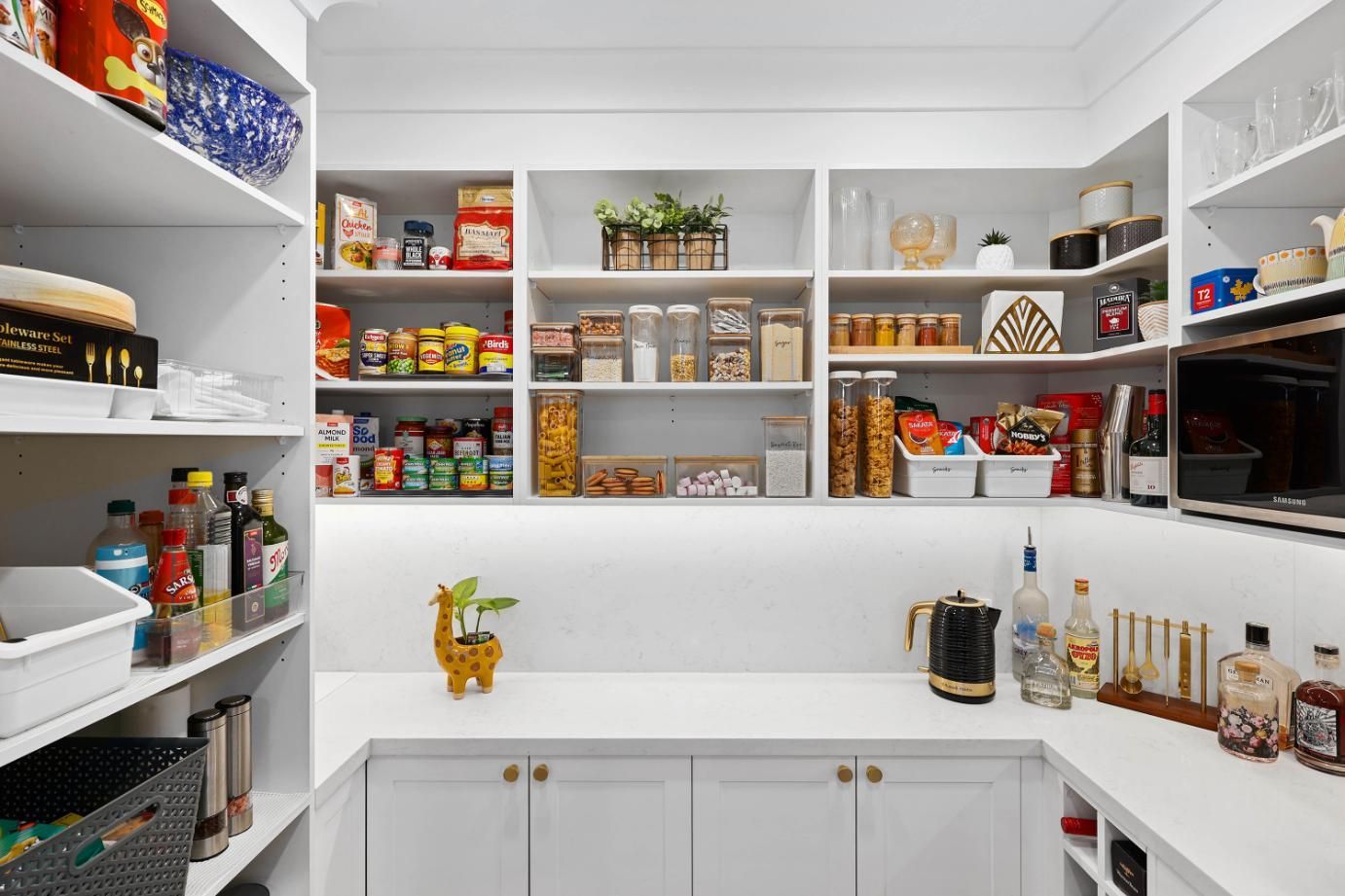 White Pantry with Shelves Filled with Food Items, a Countertop, and A Small Giraffe Statue — Above & Beyond Interiors Custom Joinery in Harrington Park, NSW