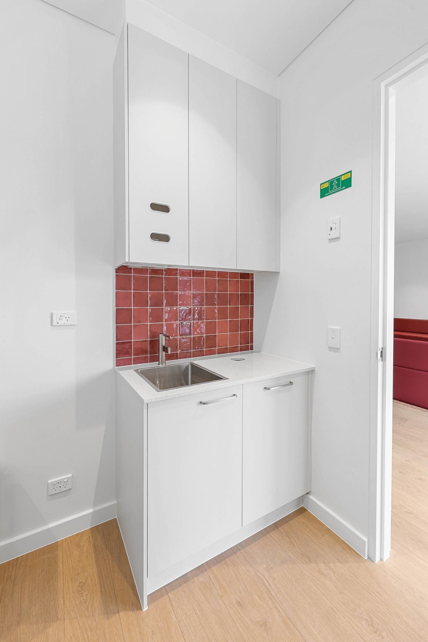 White Laundry Nook with Sink and Red Backsplash, White Cabinets, and Wood Floor — Above & Beyond Interiors Custom Joinery in Medical Centre, NSW