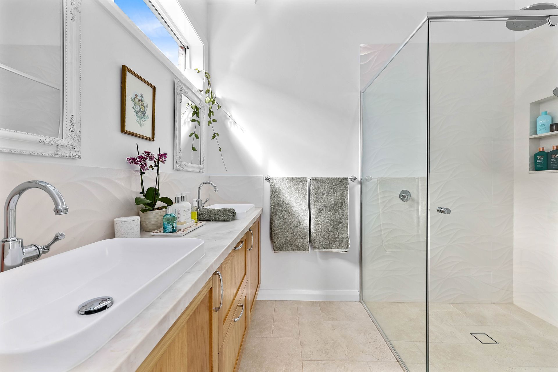 Bathroom with double sinks, glass shower, and light wood vanity. White walls, light tan flooring — Above & Beyond Interiors Custom Joinery in Bradbury, NSW