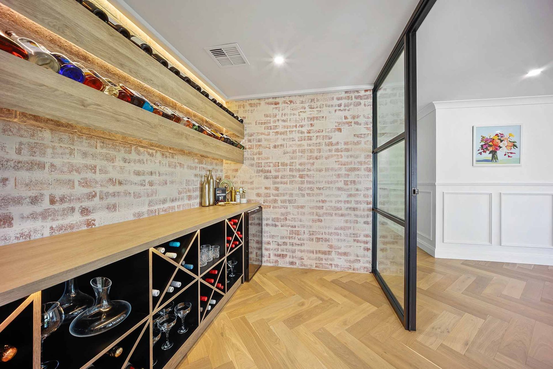 Wine cellar with brick wall, wooden shelves holding bottles, and a glass door — Above & Beyond Interiors Custom Joinery in Bellambi, NSW
