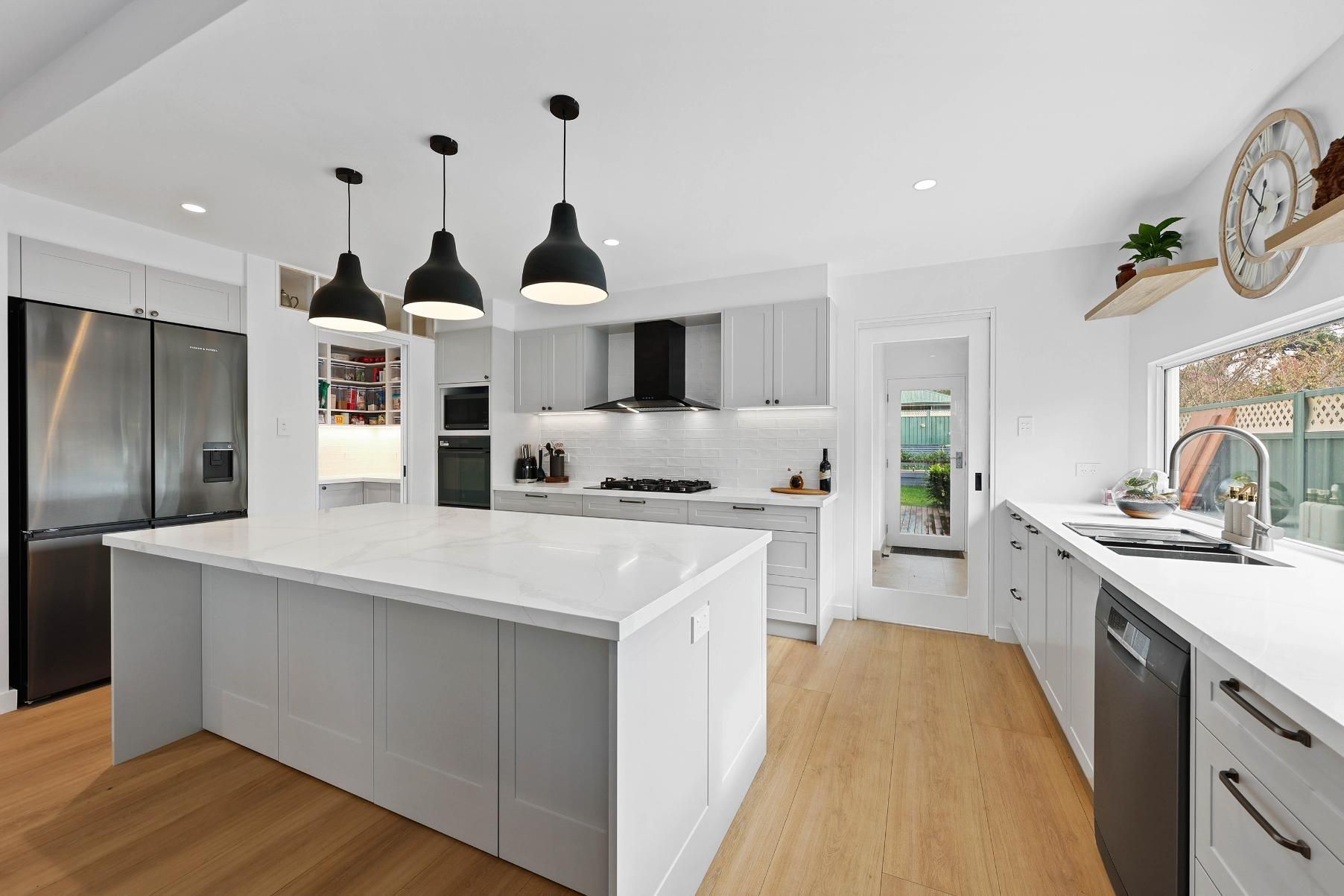 Modern White Kitchen with Island, Black Pendant Lights, Stainless Steel Appliances, and Wood Floors — Above & Beyond Interiors Custom Joinery in Yowie Bay, NSW