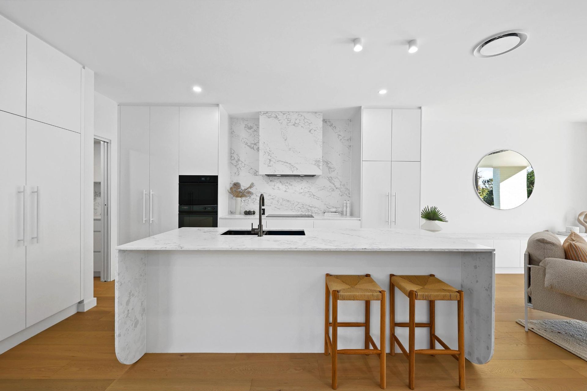White Kitchen with Marble Backsplash, Island with Stools, and Wood Floor — Above & Beyond Interiors Custom Joinery in Thirroul, NSW