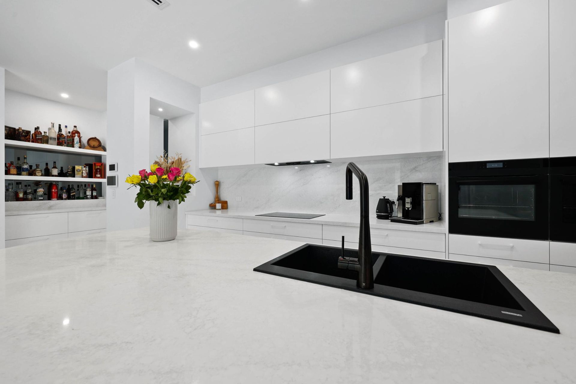 Modern White Kitchen with Black Sink and Faucet, Oven, Cabinets, and A Colorful Flower Arrangement — Above & Beyond Interiors Custom Joinery in Currans Hill, NSW