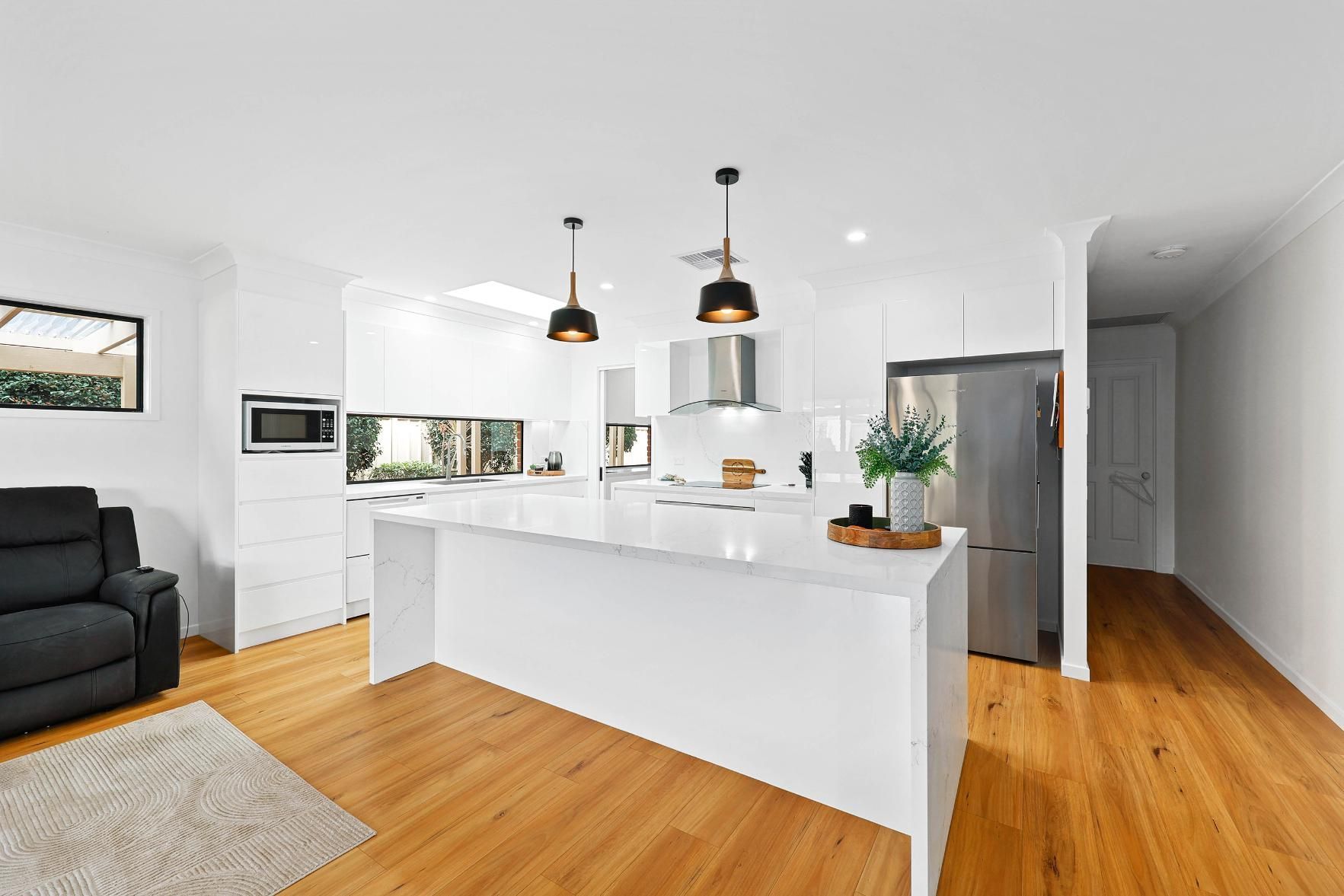 Modern White Kitchen with Island, Wooden Floor, and Pendant Lights — Above & Beyond Interiors Custom Joinery in Wattle Grove, NSW