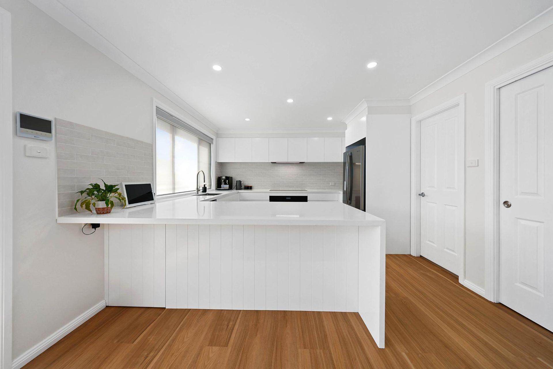 Modern White Kitchen with A Wooden Floor and White Cabinets — Above & Beyond Interiors Custom Joinery in Mount Anna, NSW
