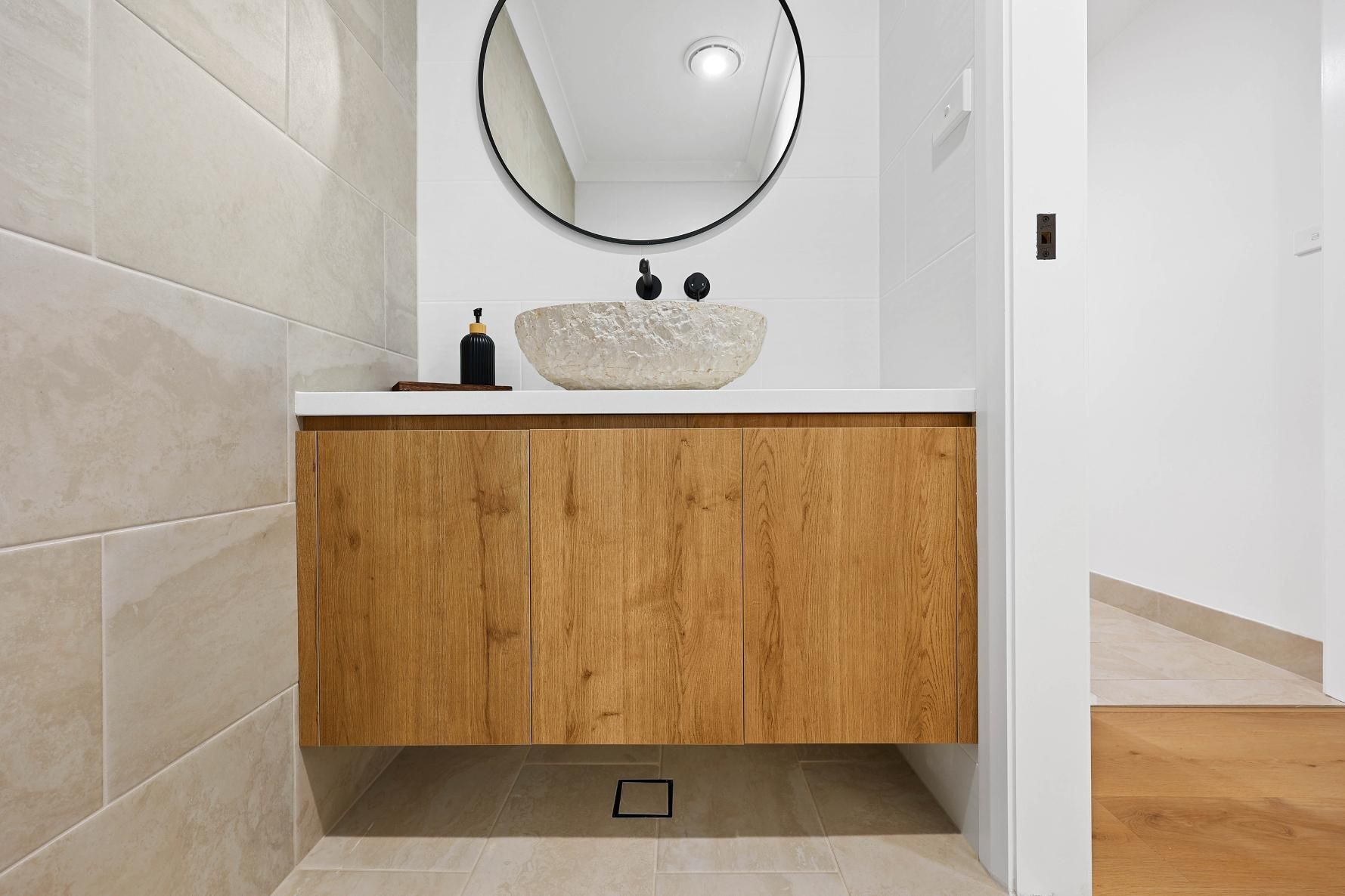 Bathroom with A Floating Wood Vanity, Stone Sink, and Round Mirror — Above & Beyond Interiors Custom Joinery in Abbortsbury, NSW