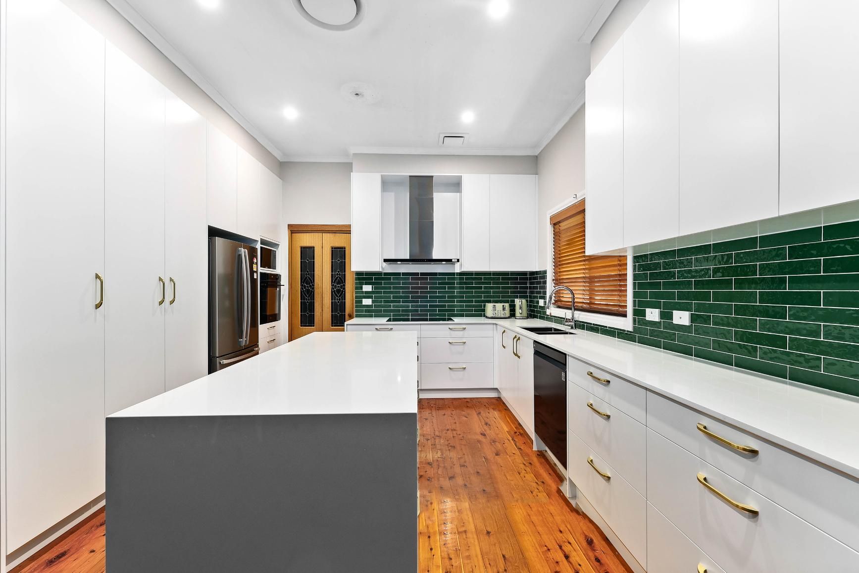 Modern White Kitchen with Green Backsplash, Island, Hardwood Floor, and Stainless Steel Appliances — Above & Beyond Interiors Custom Joinery in Minto, NSW