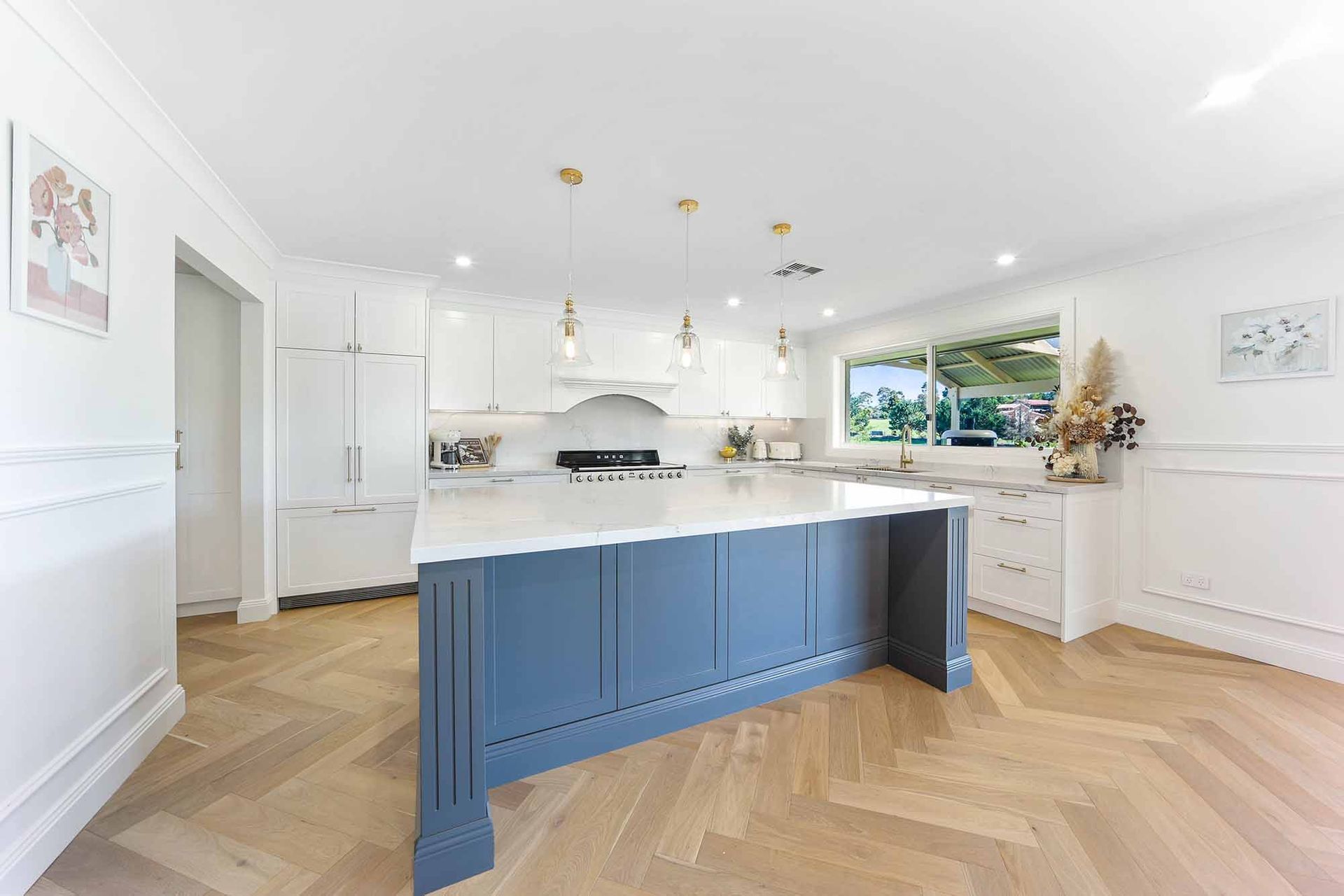 Kitchen with blue island, white cabinets, gold light fixtures, and herringbone wood floors — Above & Beyond Interiors Custom Joinery in Bellambi, NSW