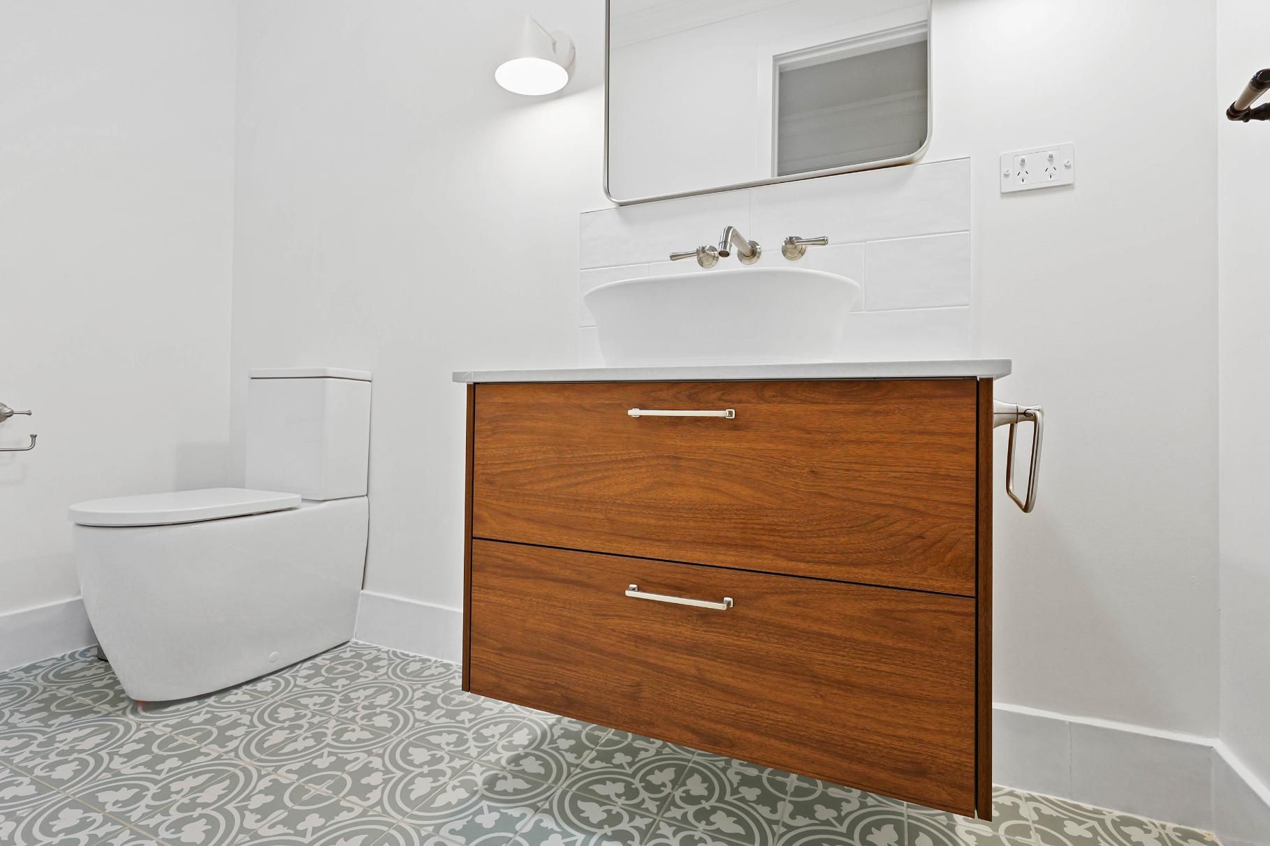 Modern Bathroom with A Wooden Vanity, White Toilet, and Patterned Grey Floor Tiles — Above & Beyond Interiors Custom Joinery in Appin, NSW