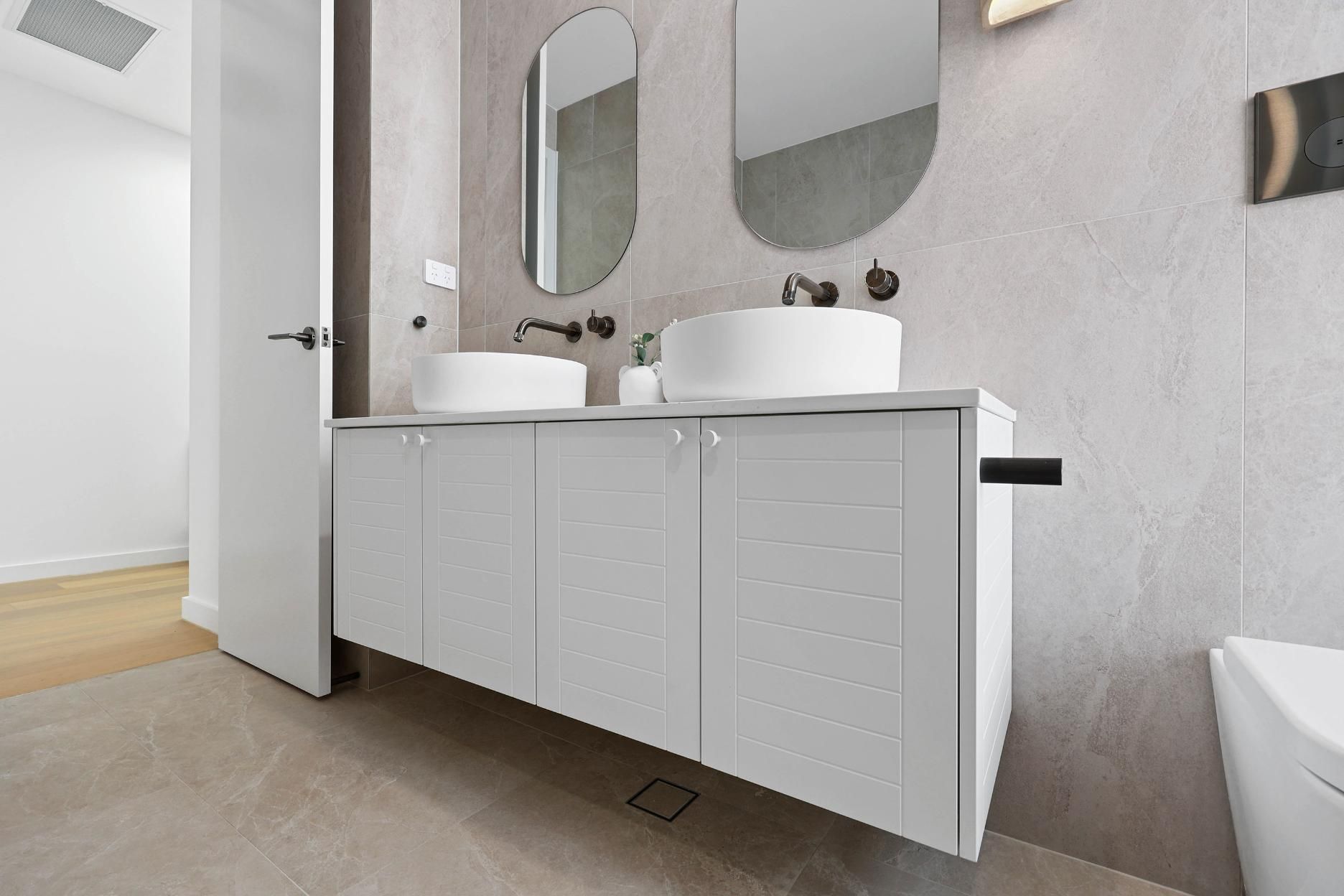 Bathroom with White Vanity, Round Sinks, Oval Mirrors, Neutral Walls, and Light-Colored Floors — Above & Beyond Interiors Custom Joinery in Thirroul, NSW