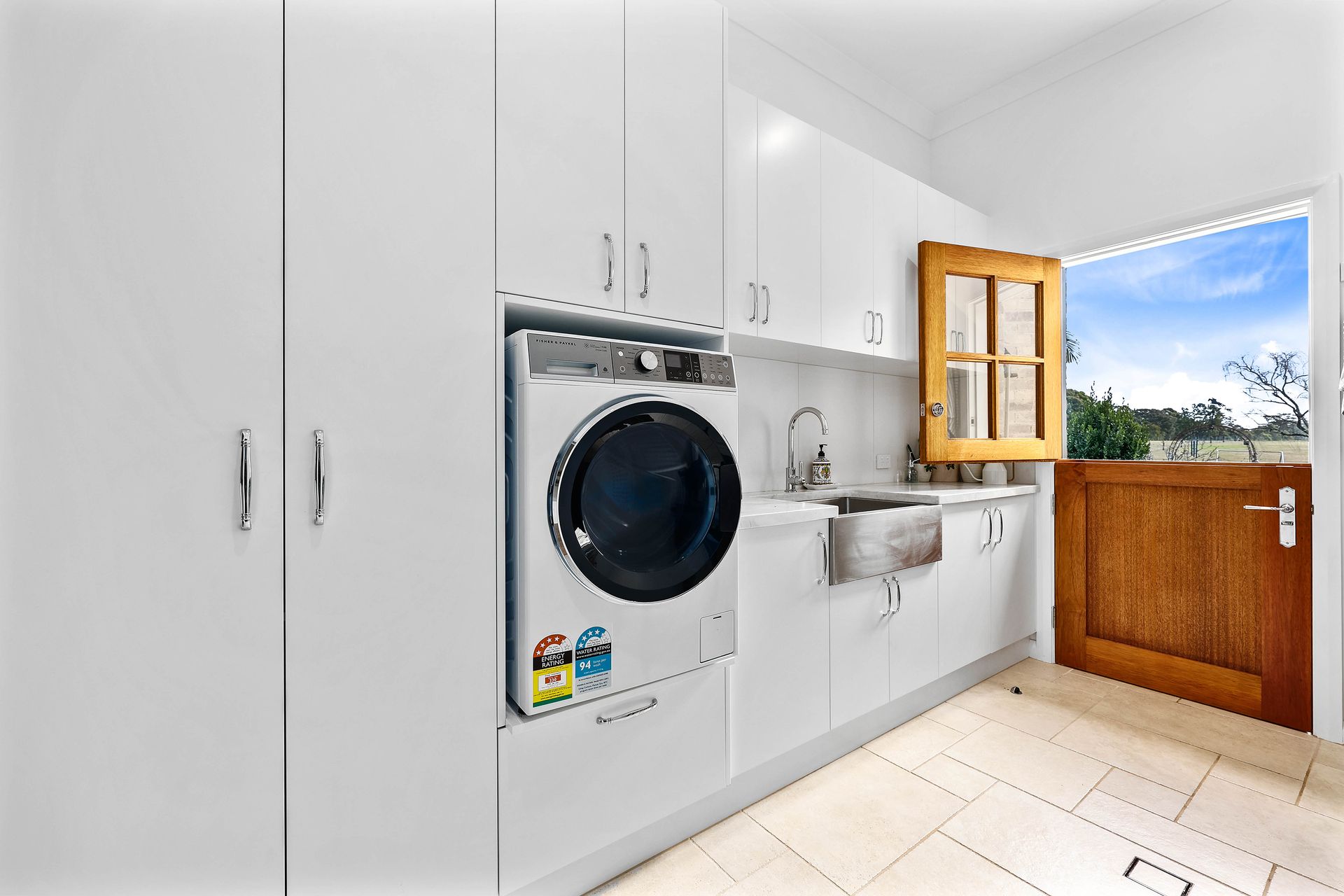 Laundry room with white cabinets, washing machine, and a half-open wooden door to the outside — Above & Beyond Interiors Custom Joinery in Bradbury, NSW