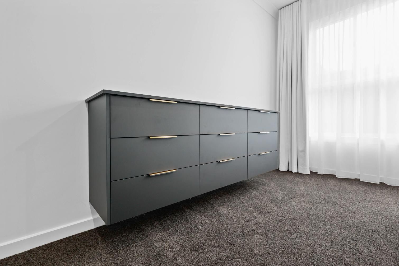 Grey Floating Cabinet with Gold Handles, Against a White Wall and Carpeted Floor — Above & Beyond Interiors Custom Joinery in Currans Hill, NSW