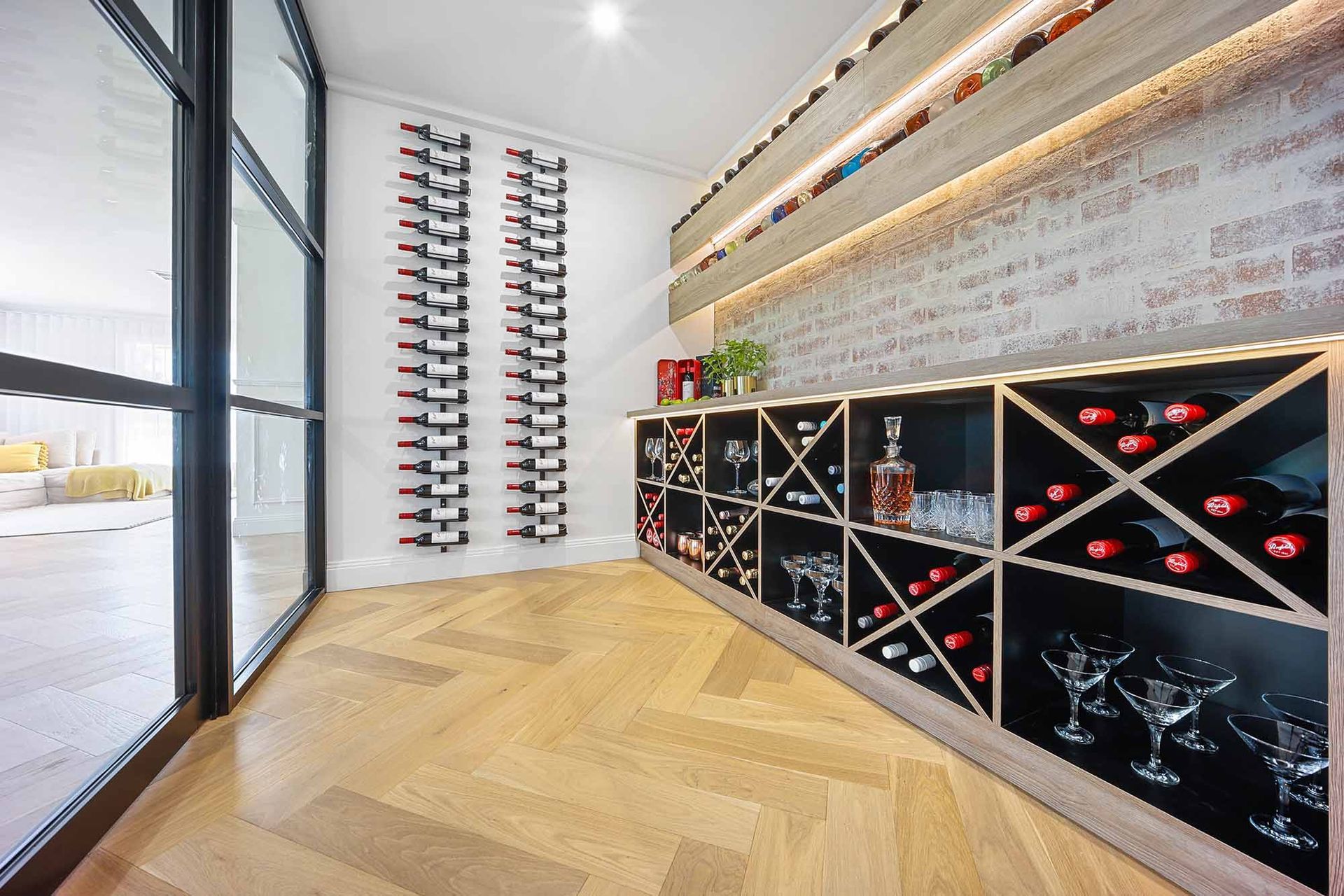 Wine cellar with wood floors, shelves holding bottles. Glass door — Above & Beyond Interiors Custom Joinery in Bellambi, NSW