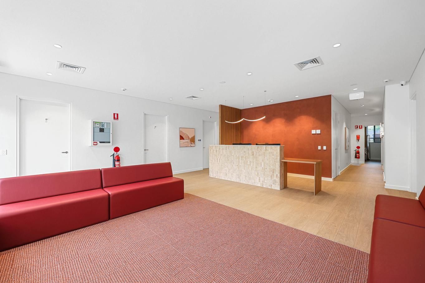 Lobby with Red Couches, a Reception Desk with A Textured Front, and An Orange Accent Wall — Above & Beyond Interiors Custom Joinery in Medical Centre, NSW