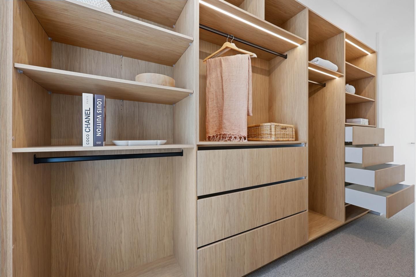 Wooden Walk-In Closet with Shelves, Drawers, Hanging Rod, and Built-In Lighting. Contains Clothing and Decorative Items — Above & Beyond Interiors Custom Joinery in Thirroul, NSW