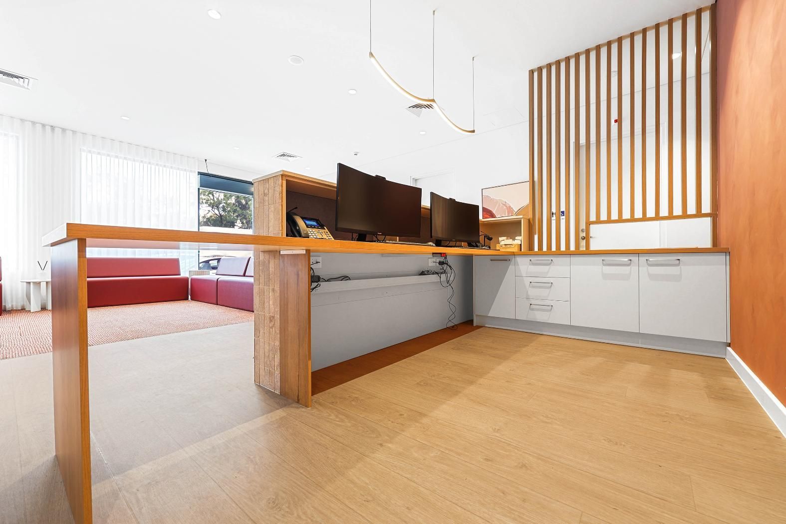 An Office Space with A Wooden Desk, Three Monitors, and White Cabinets. the Floor Is Light Wood — Above & Beyond Interiors Custom Joinery in Medical Centre, NSW