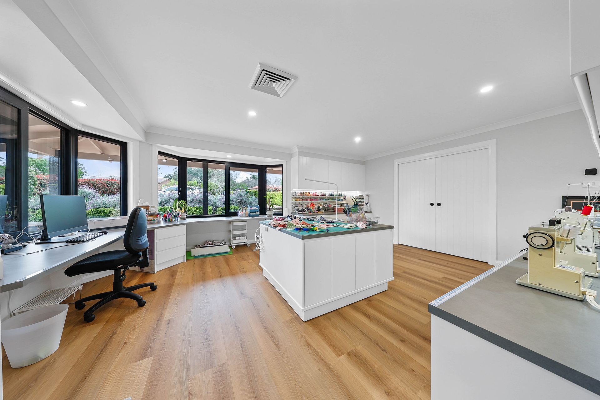 Bright, modern workspace with a central island, desk by a large window, and hardwood floors — Above & Beyond Interiors Custom Joinery in Bellambi, NSW