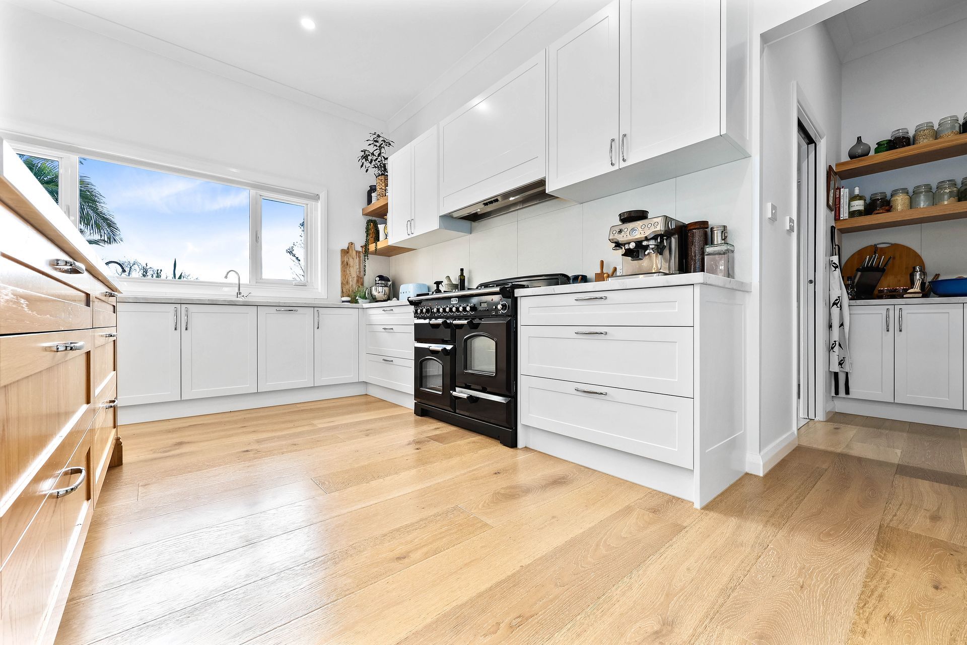 Bright white kitchen with hardwood floors, black oven, and large window — Above & Beyond Interiors Custom Joinery in Bradbury, NSW